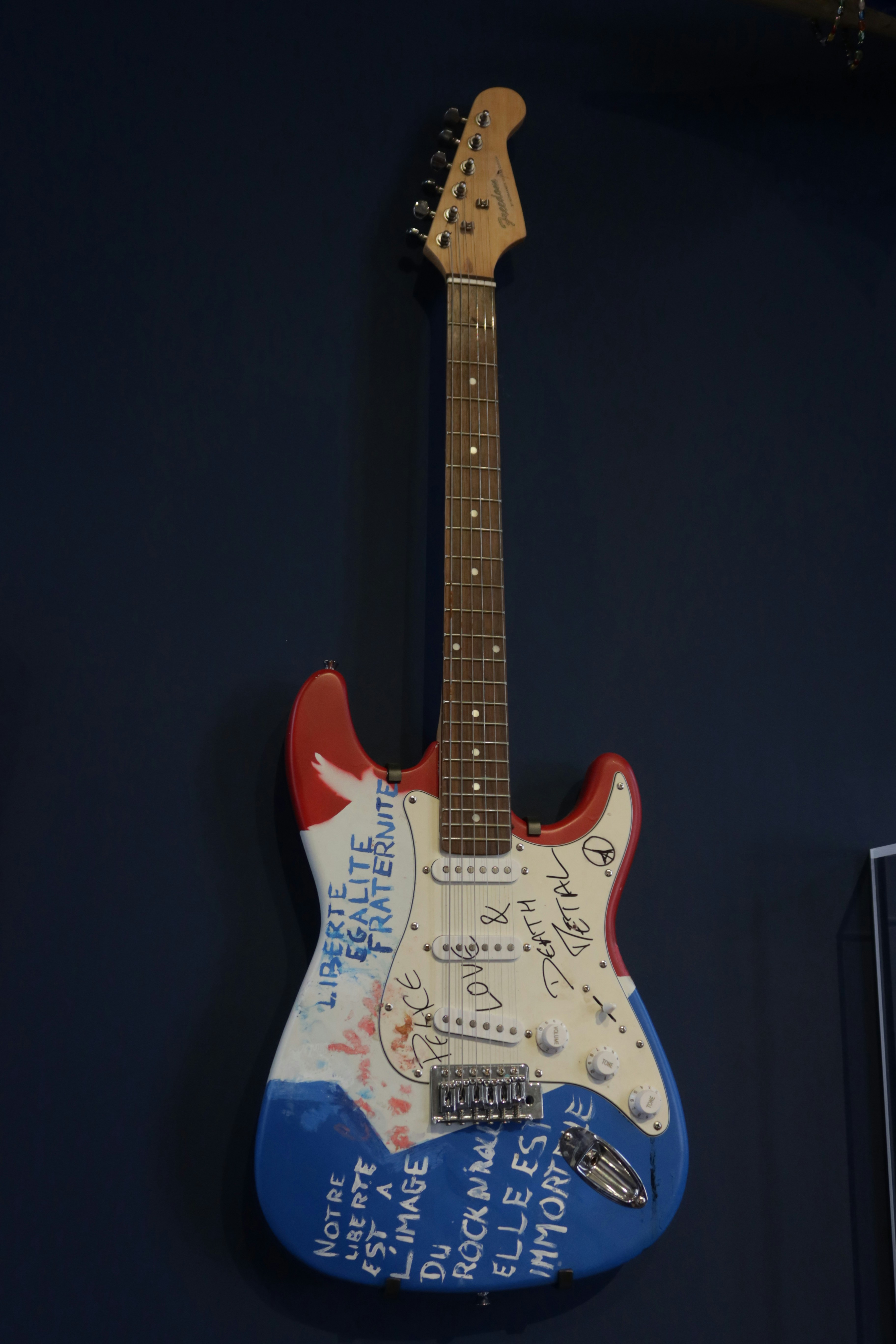 A guitar painted with french flag colors and text.
