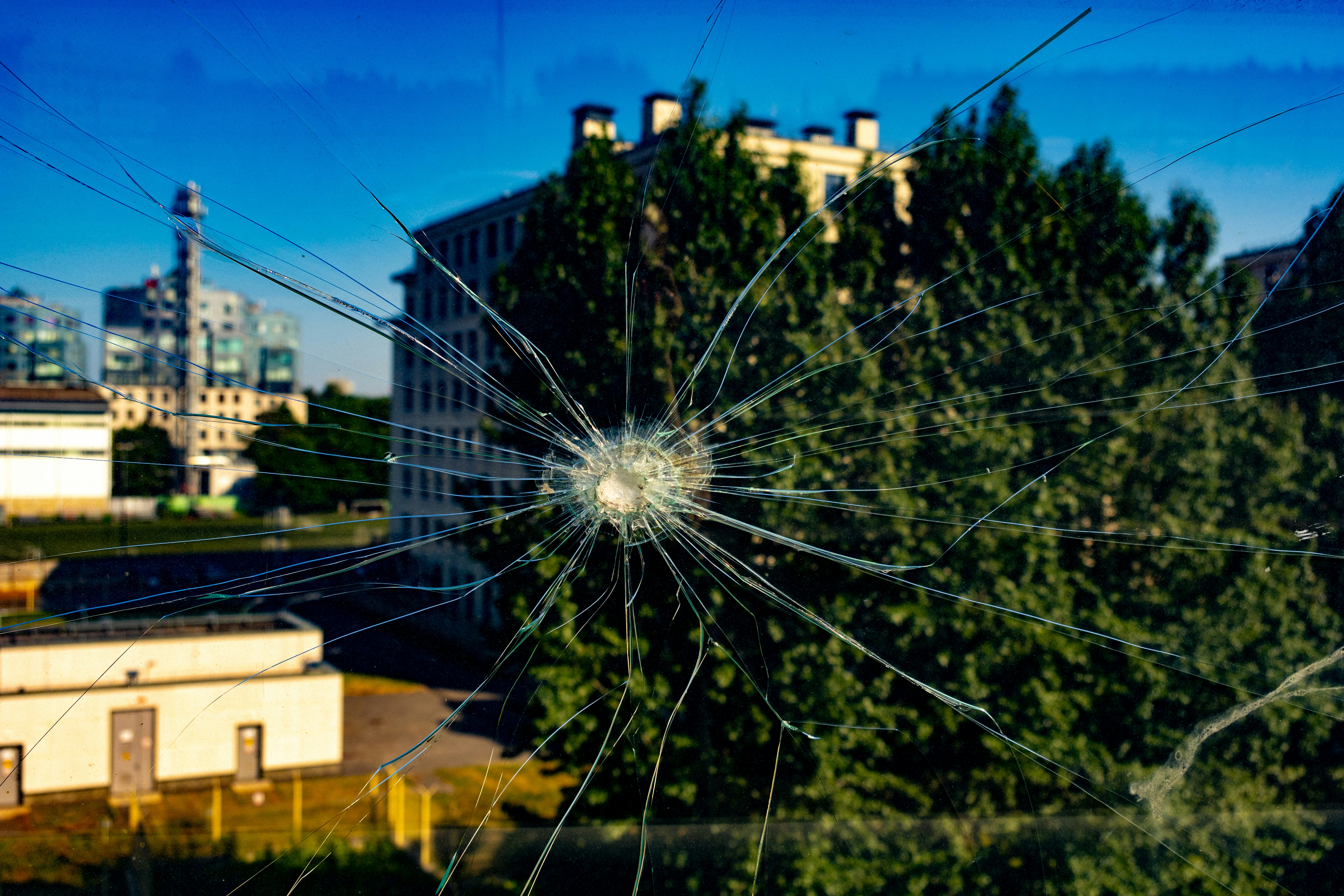 Shattered glass reveals city buildings and trees.