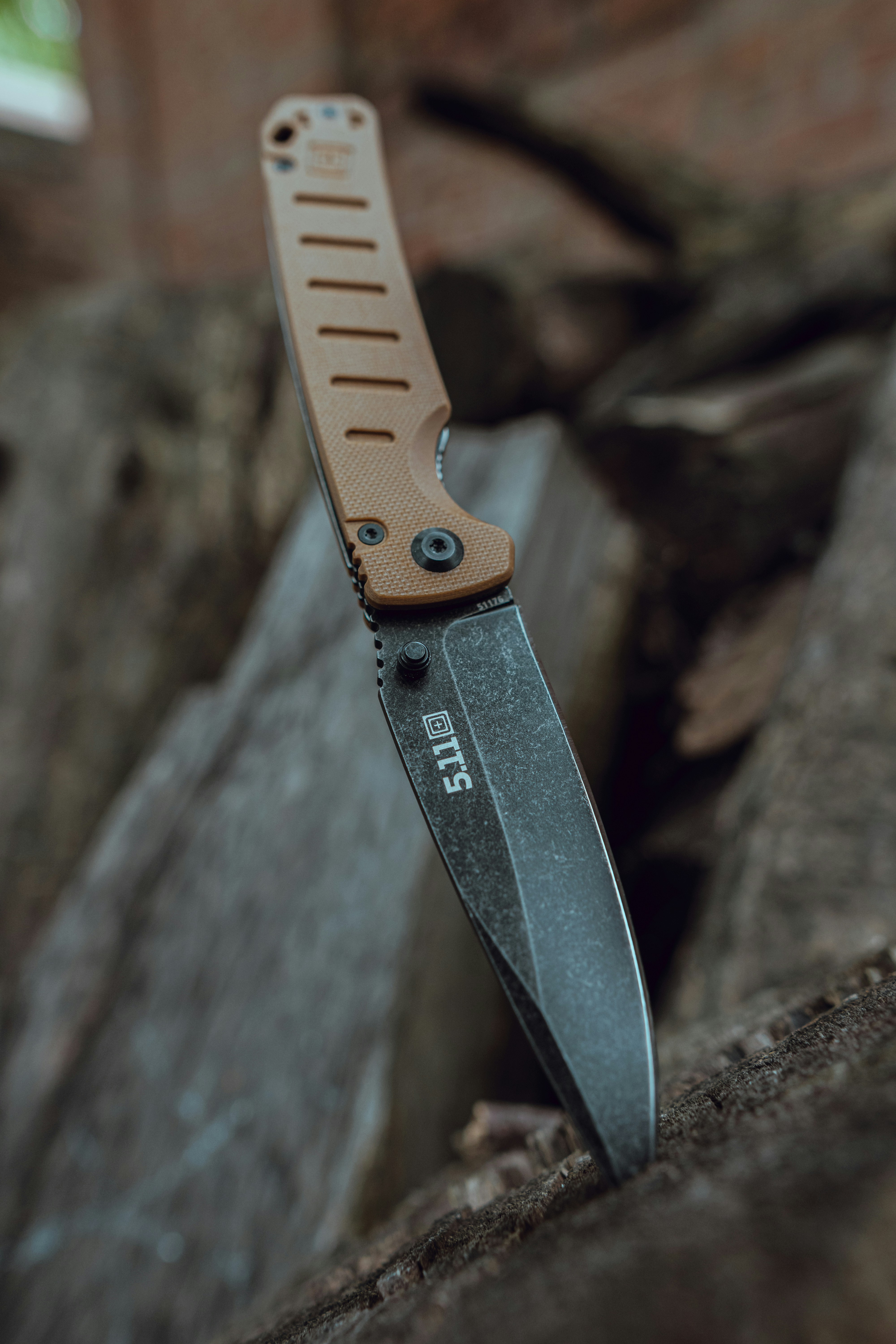 A 5.11 tactical knife is lodged in wood.