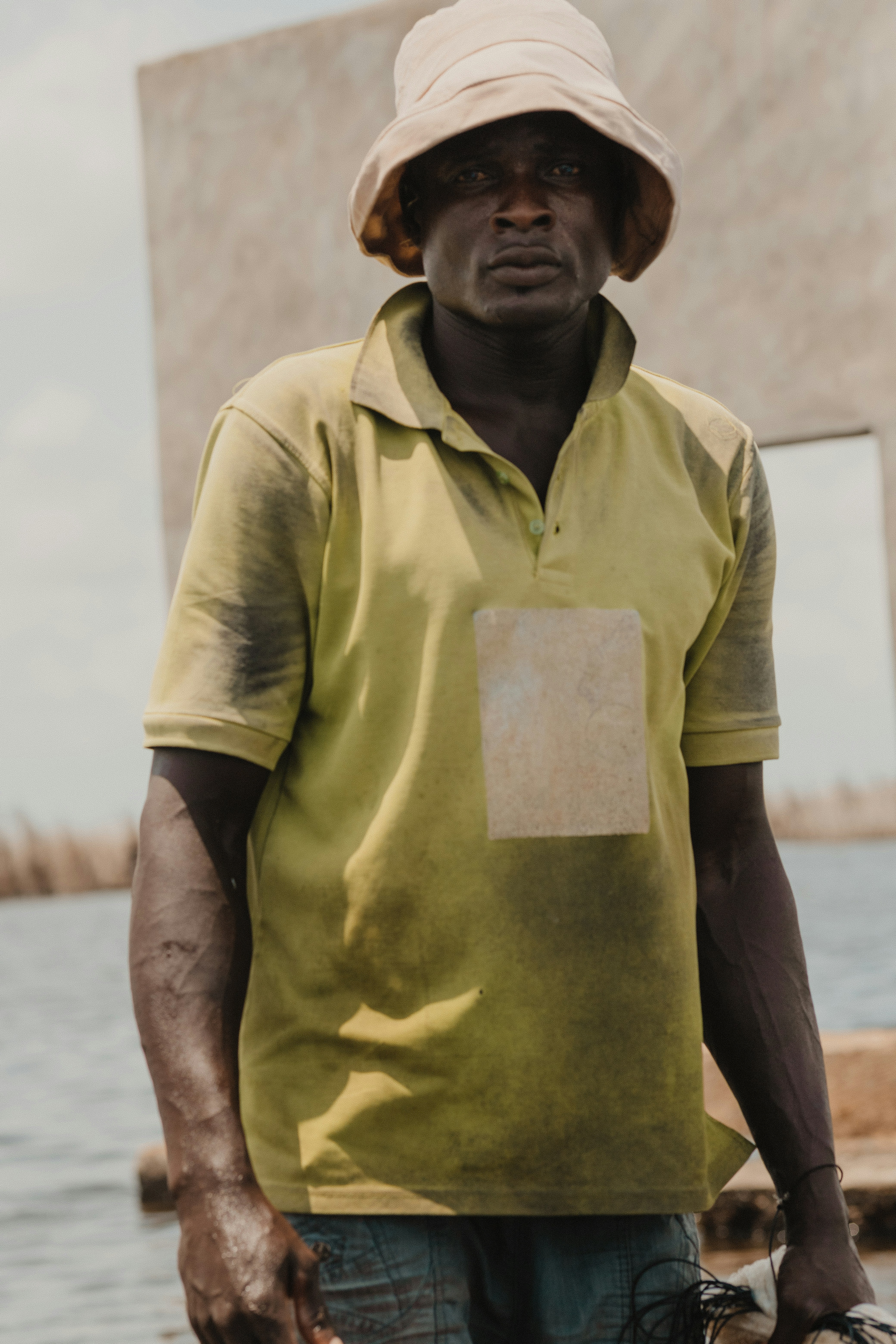 A man stands by the water wearing a hat.