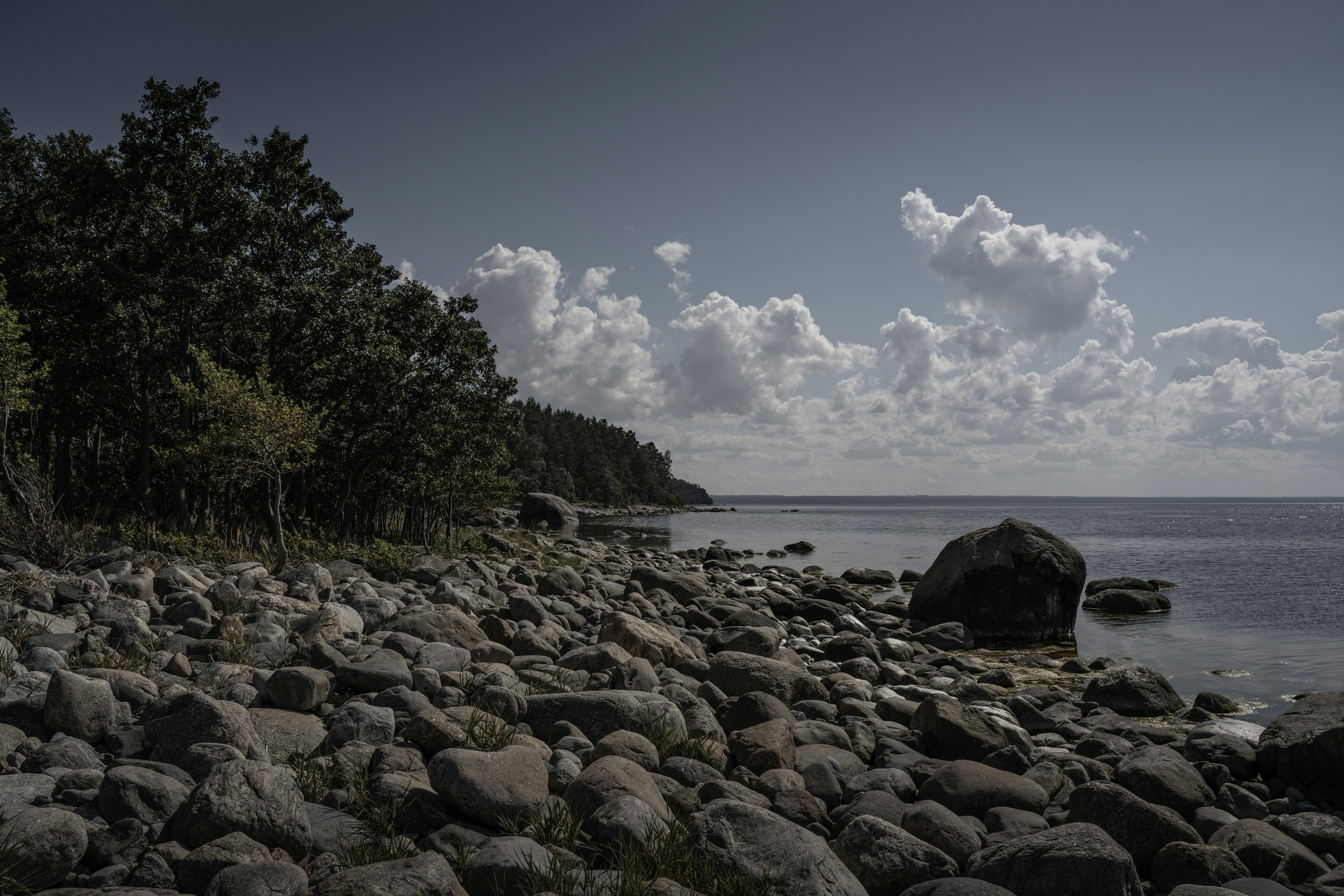 Rocky shore meets the calm sea under a cloudy sky.