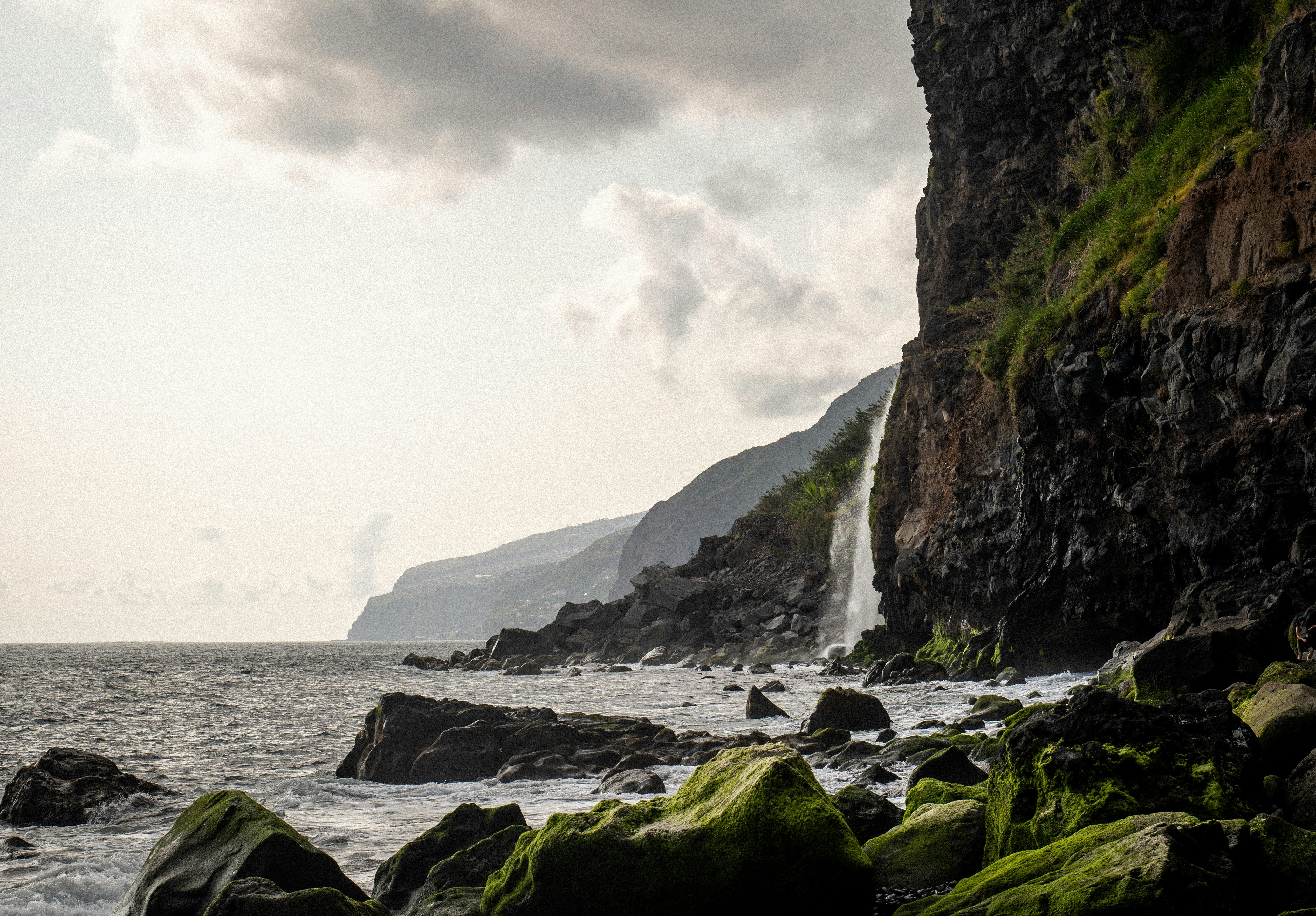 A waterfall cascades down cliffs into the sea.