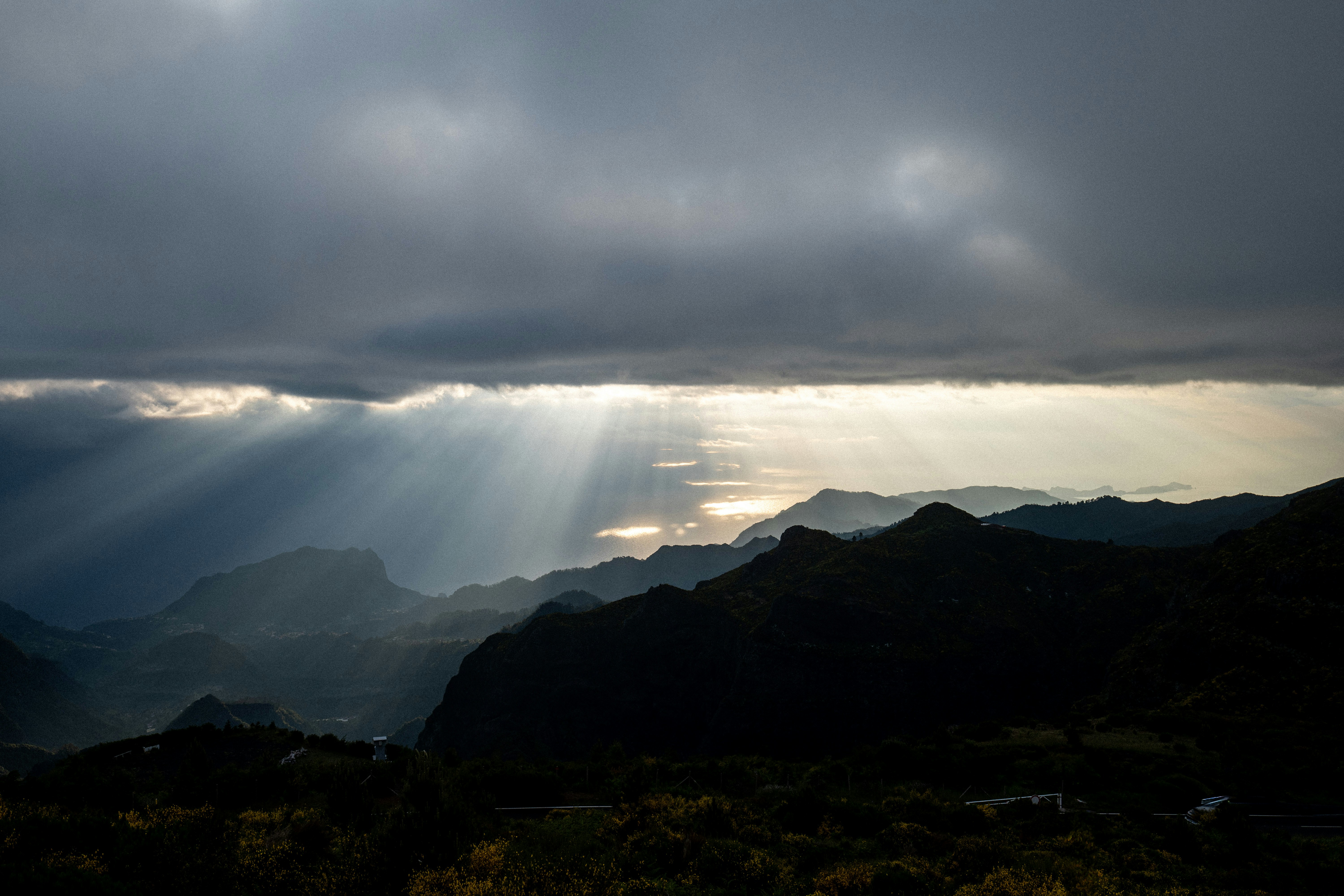 Sunlight streams through dark clouds over mountains.