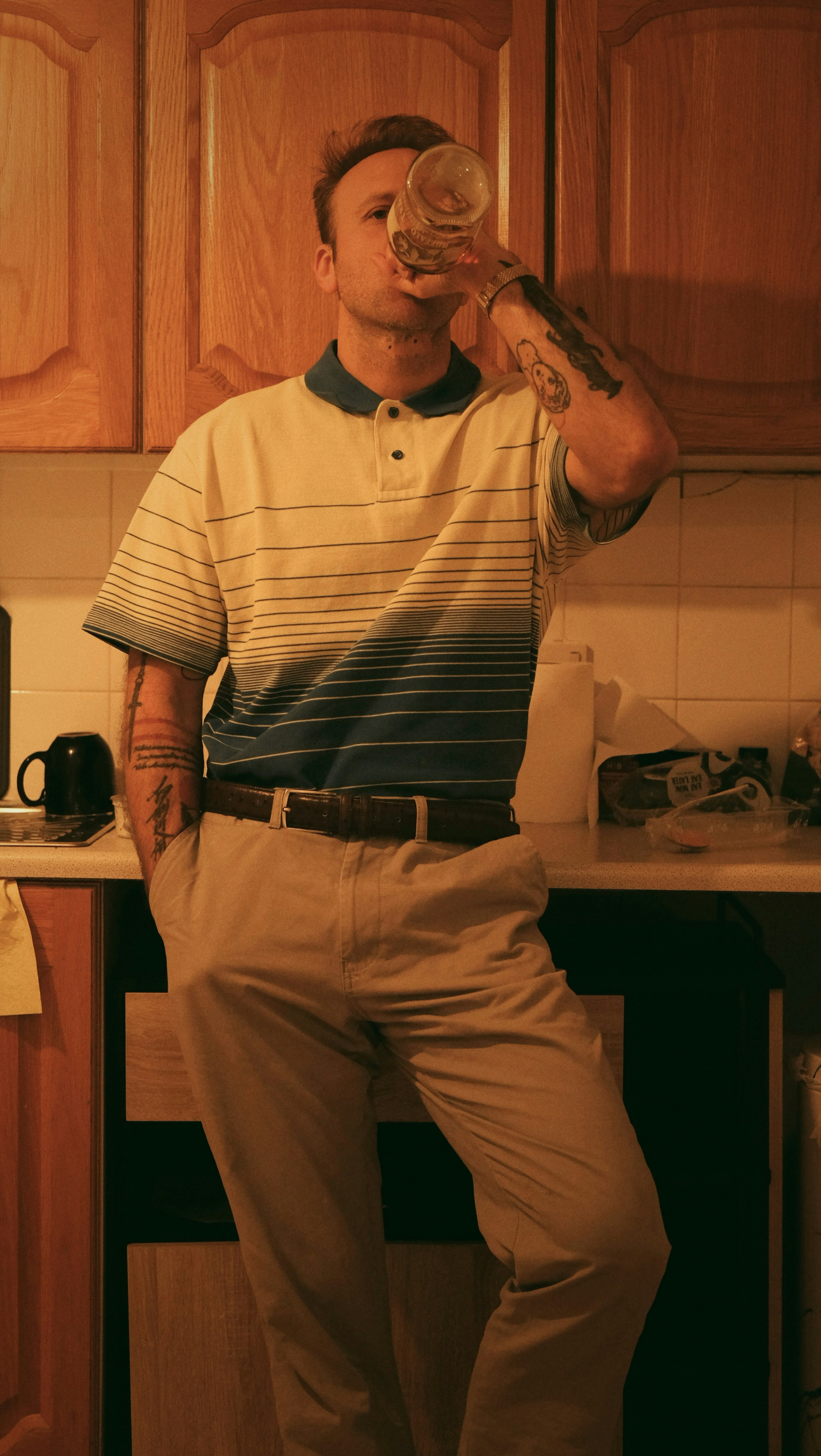 A man drinks from a glass in the kitchen.