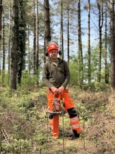 A forester stands in a forest with a chainsaw.