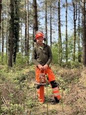 A forester stands in a forest with a chainsaw.