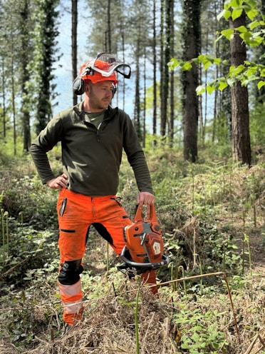 A forester poses with a chainsaw in the woods.