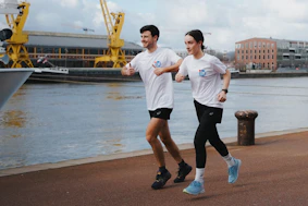 A couple is running near a waterfront.