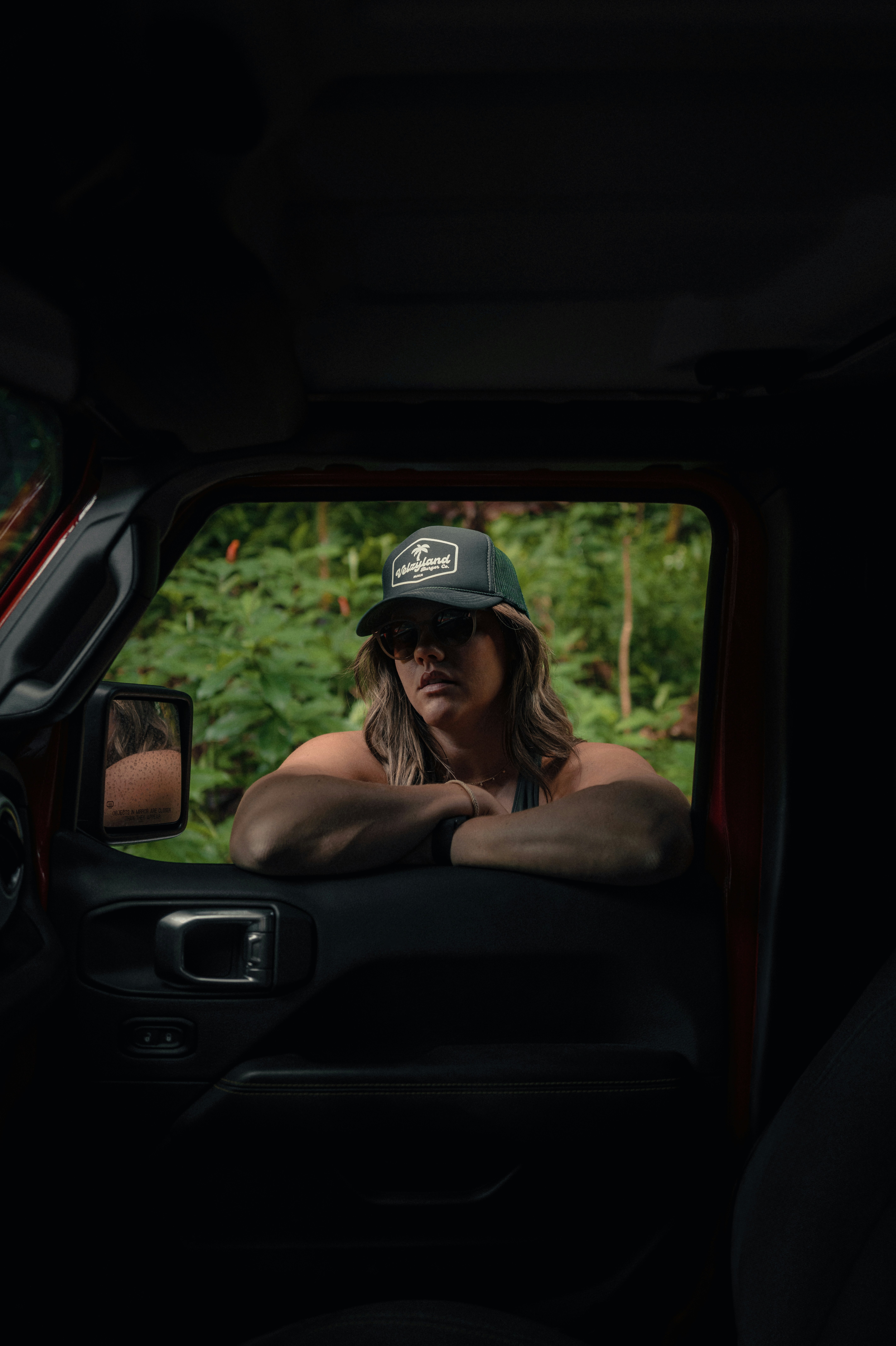 A woman leans on a car door, looking out