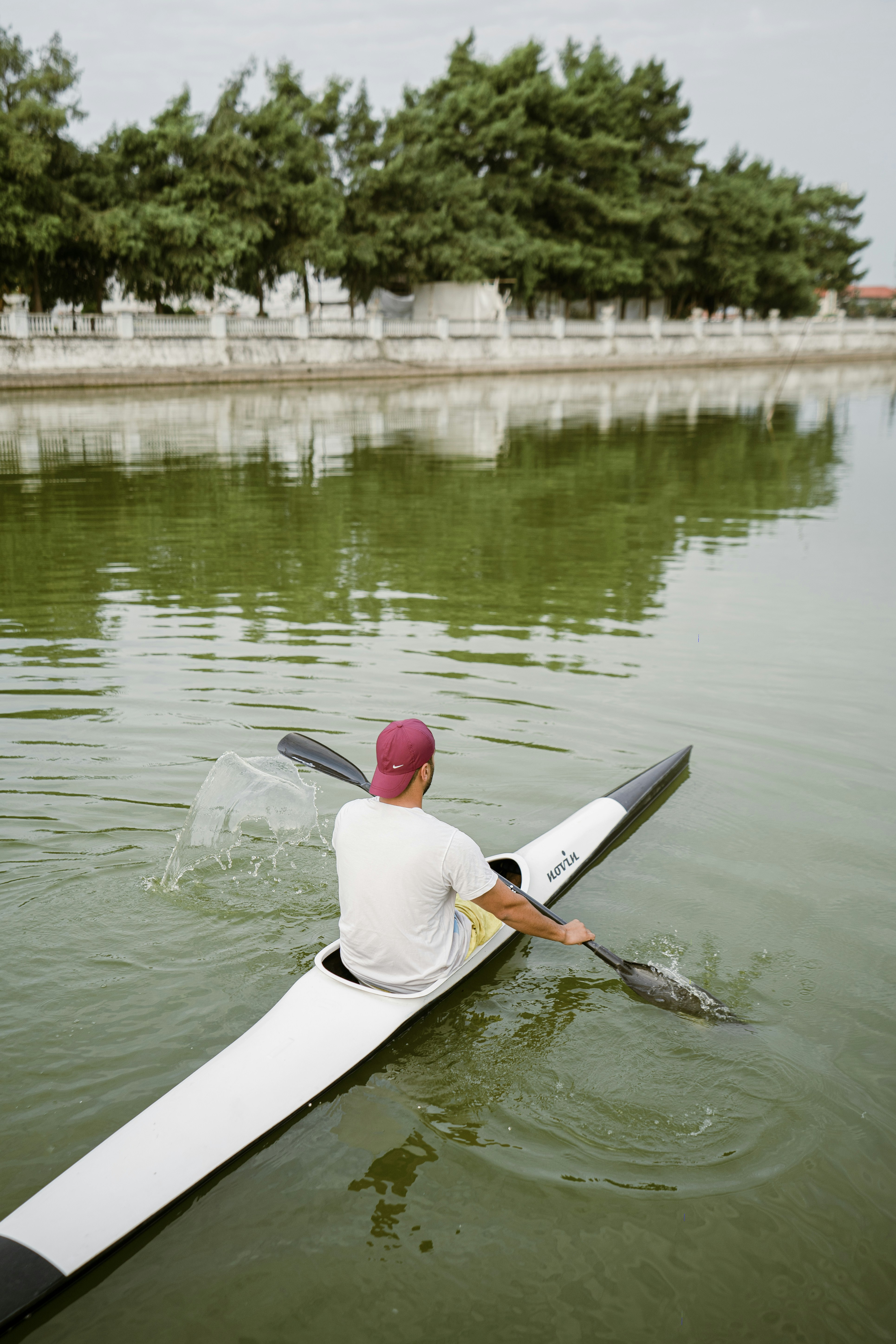 A man paddles a kayak on the calm water.