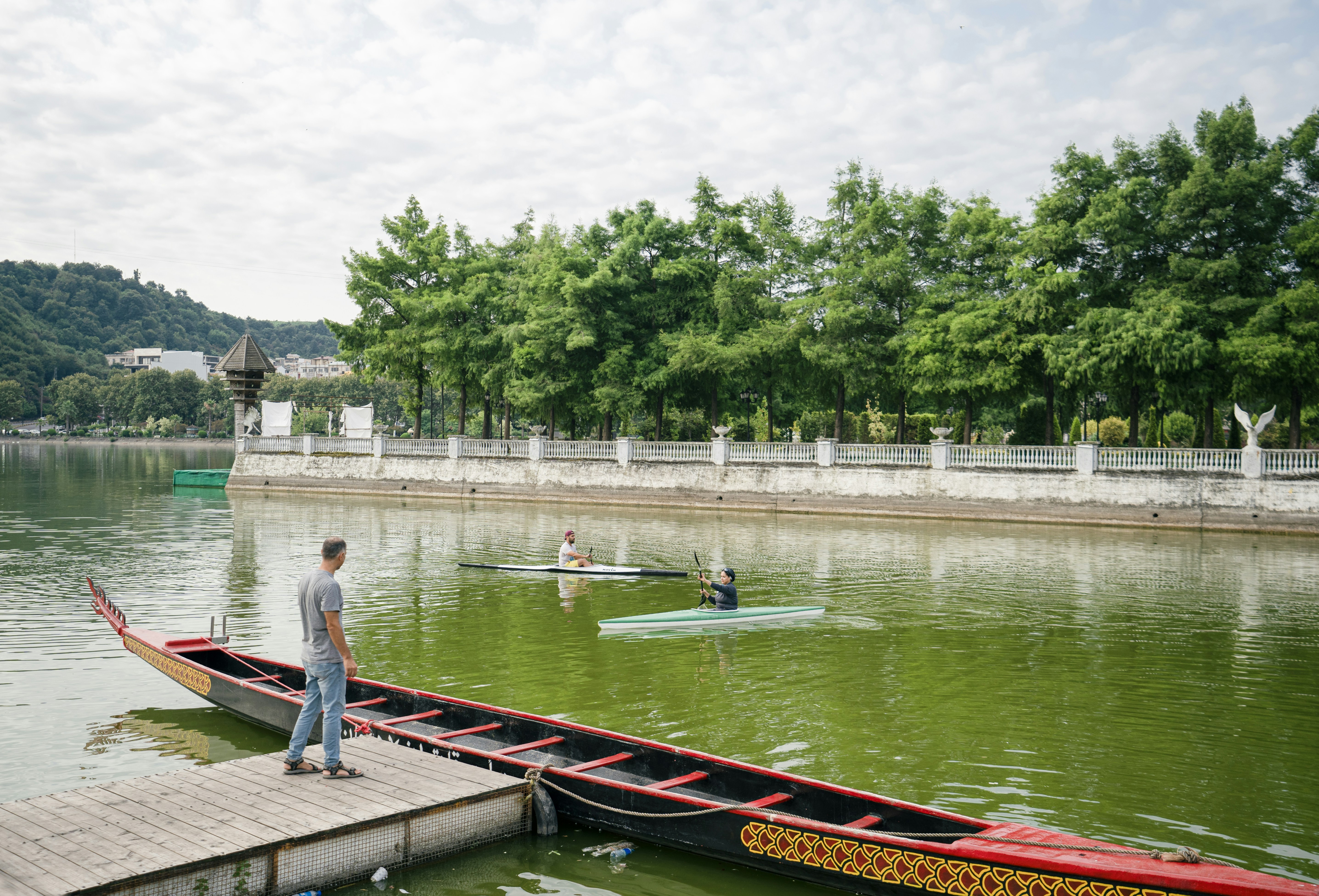 Man stands by a boat and watches kayakers.