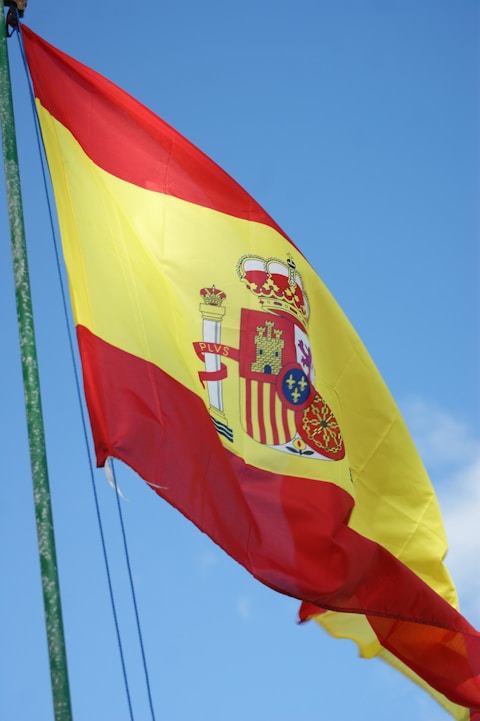The spanish flag flutters against a blue sky.