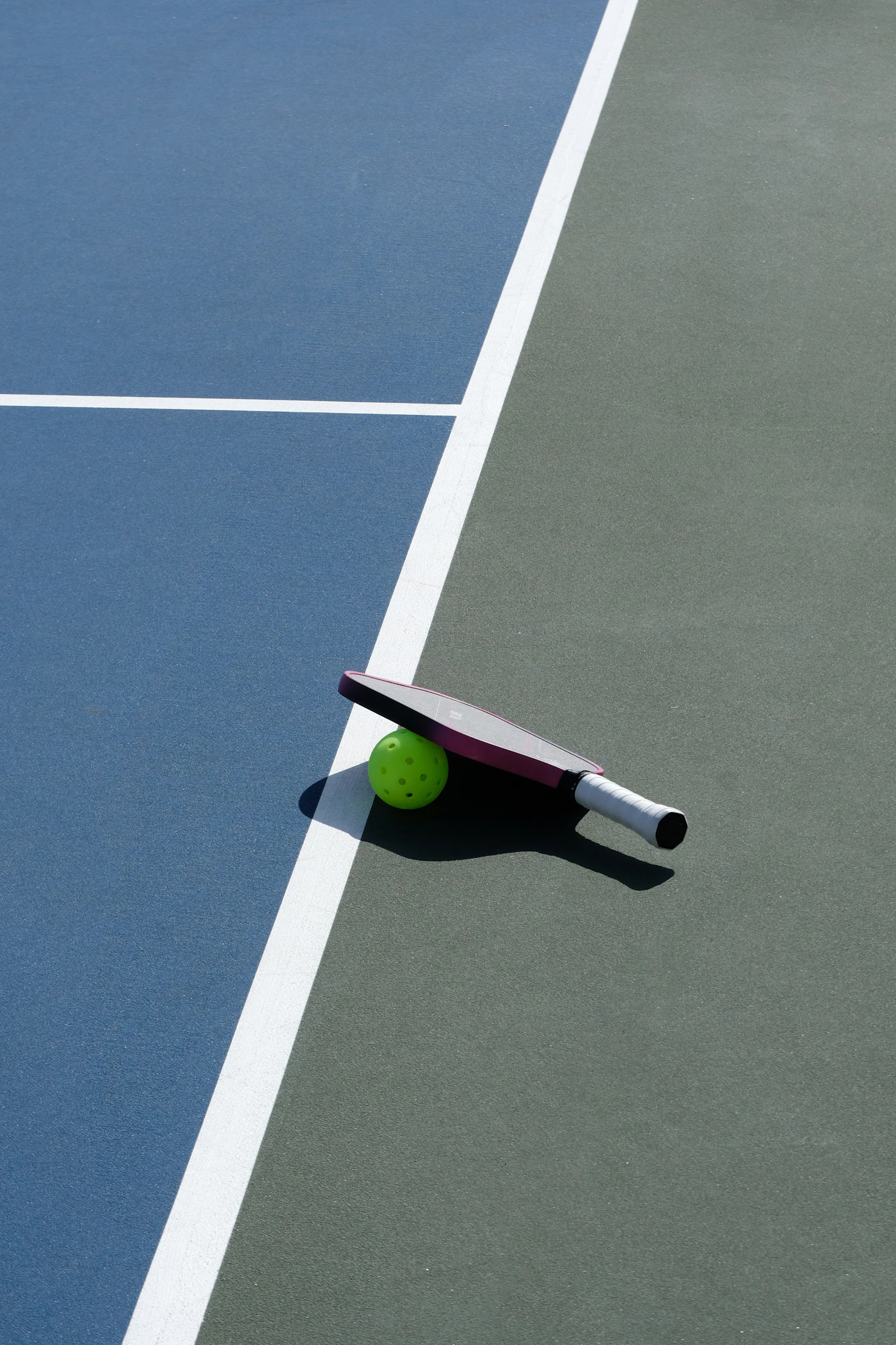 A pickleball paddle and green ball resting beside a court line.
