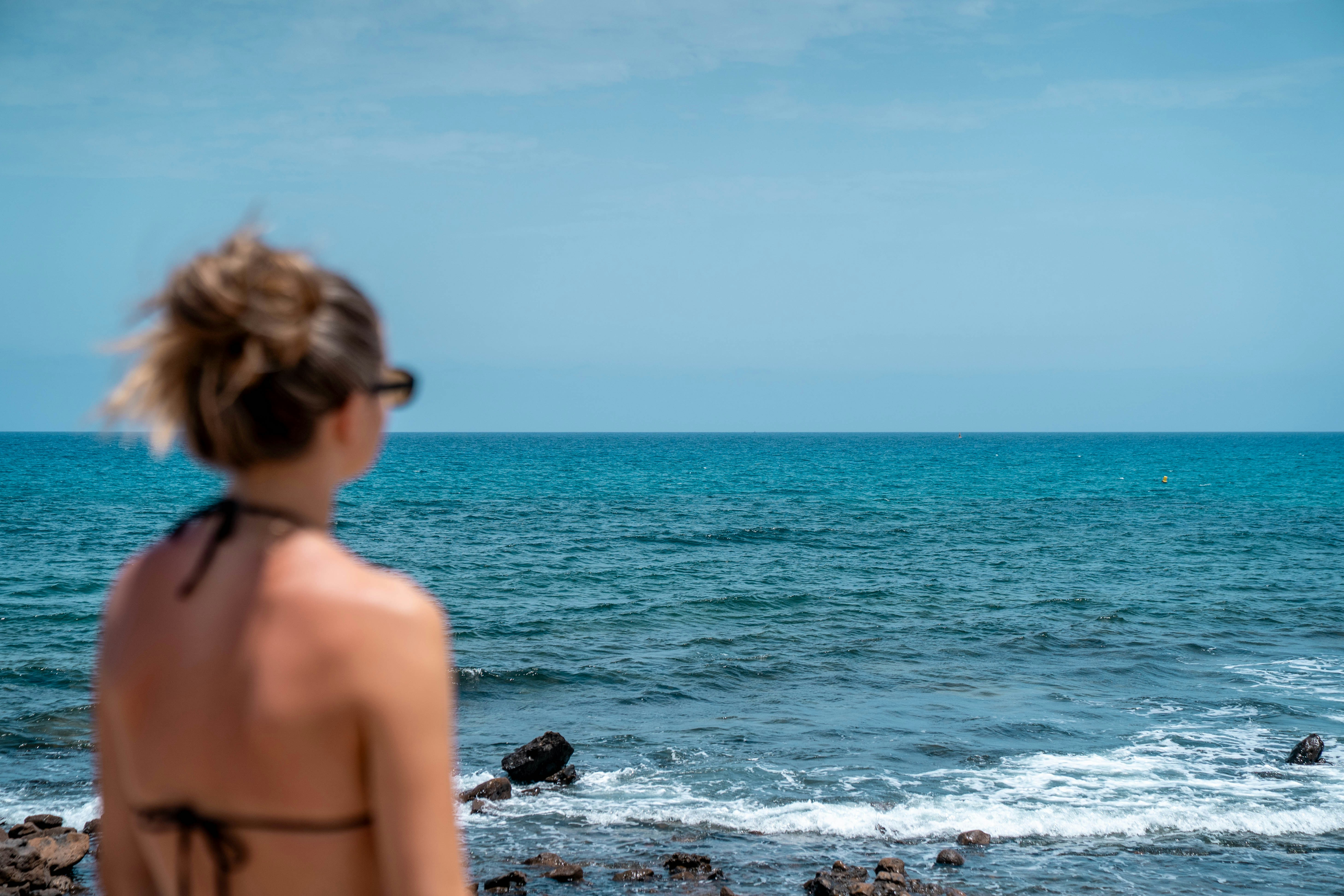 Woman looks out at the ocean on a sunny day.