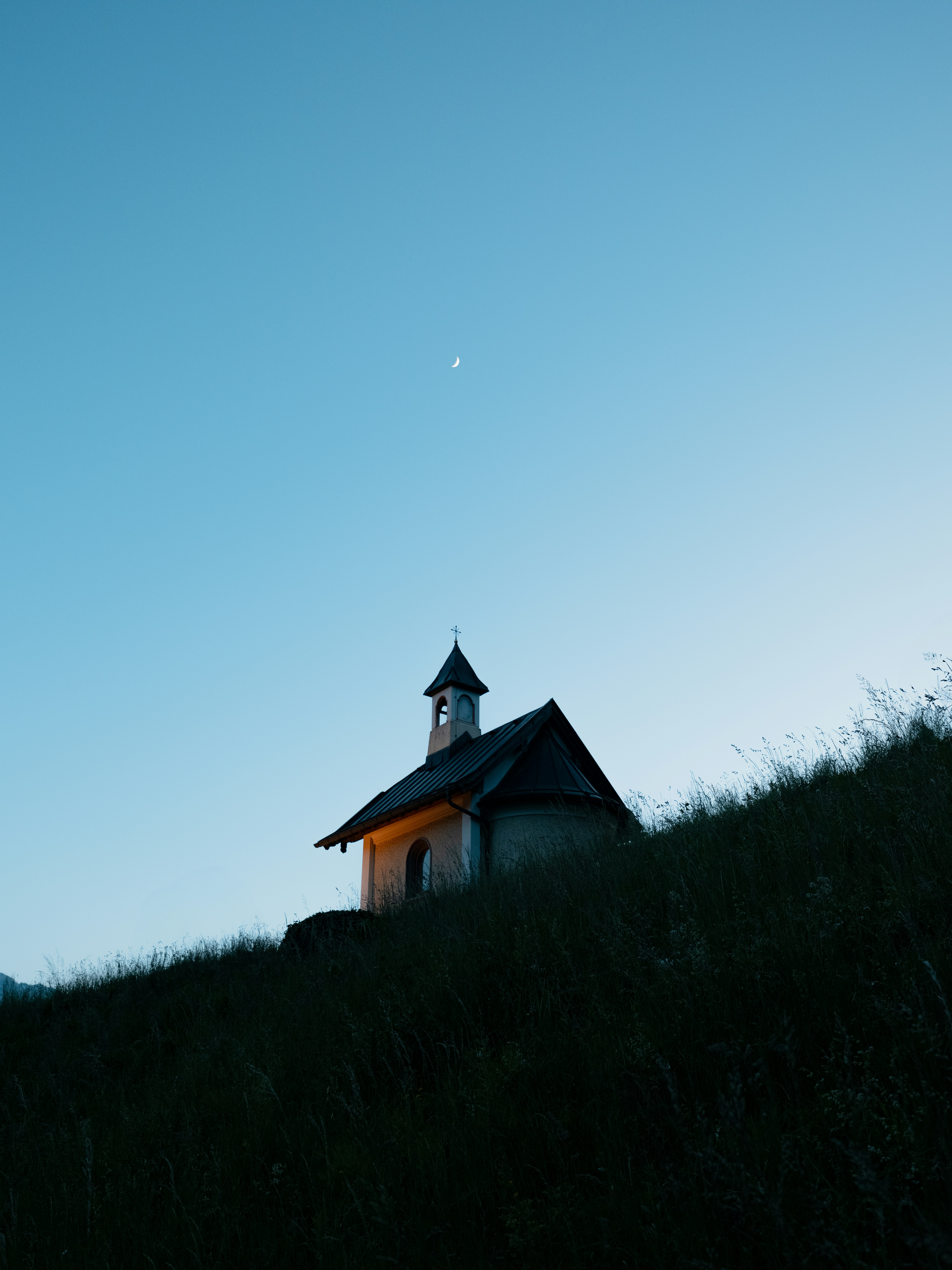 A chapel sits atop a grassy hill at dusk.