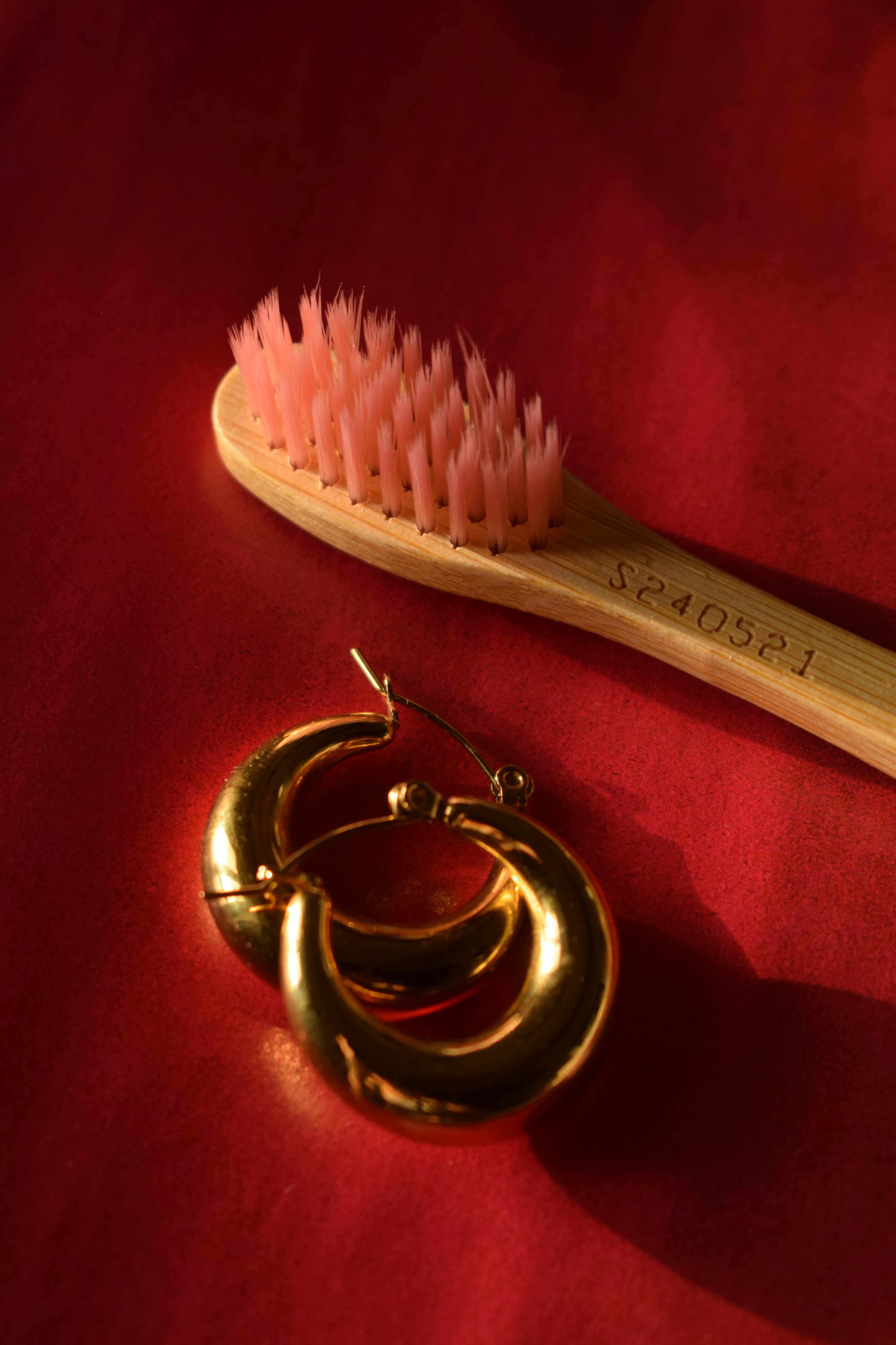 Gold earrings and a toothbrush on red.