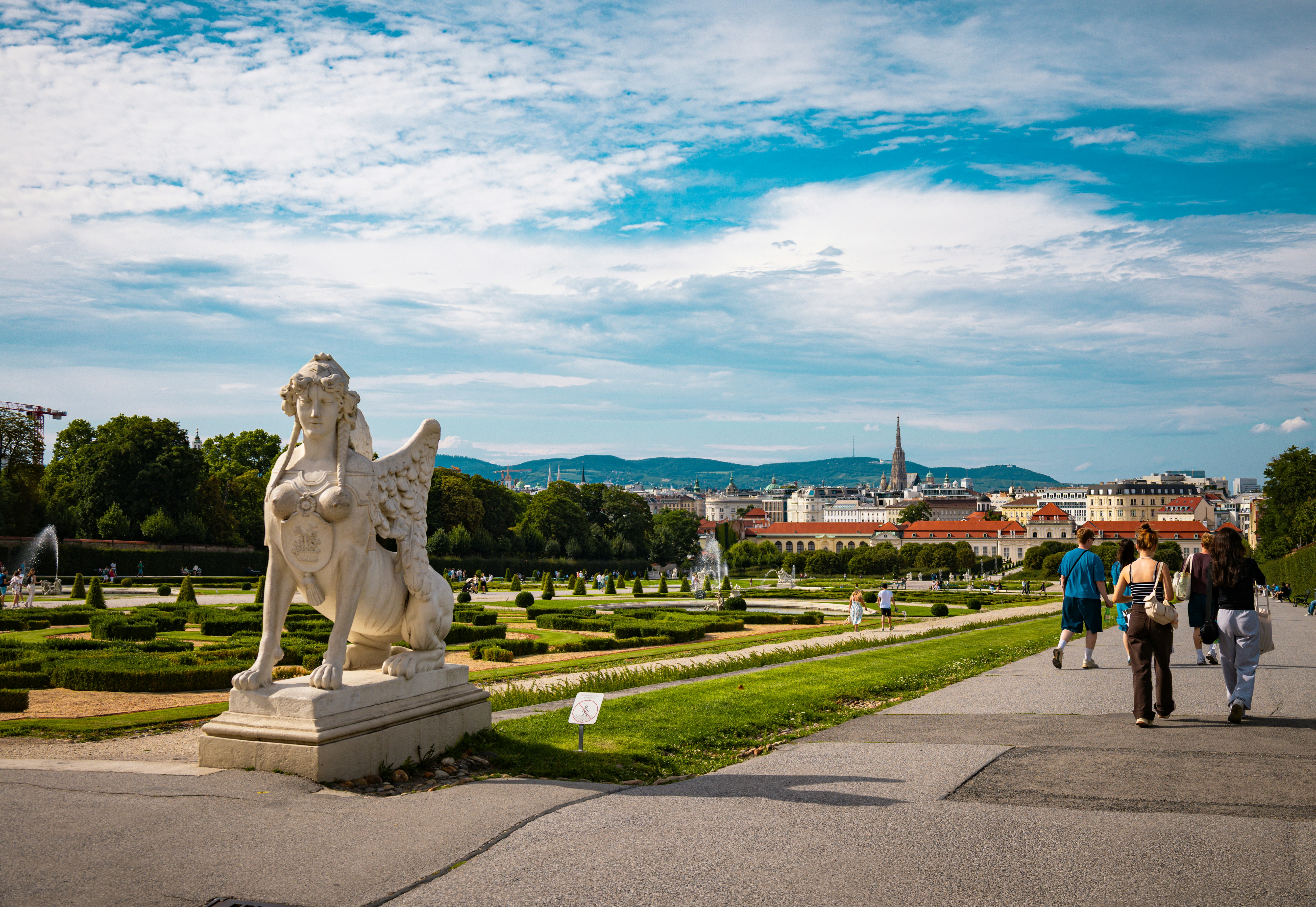 People stroll through a park with a large statue.