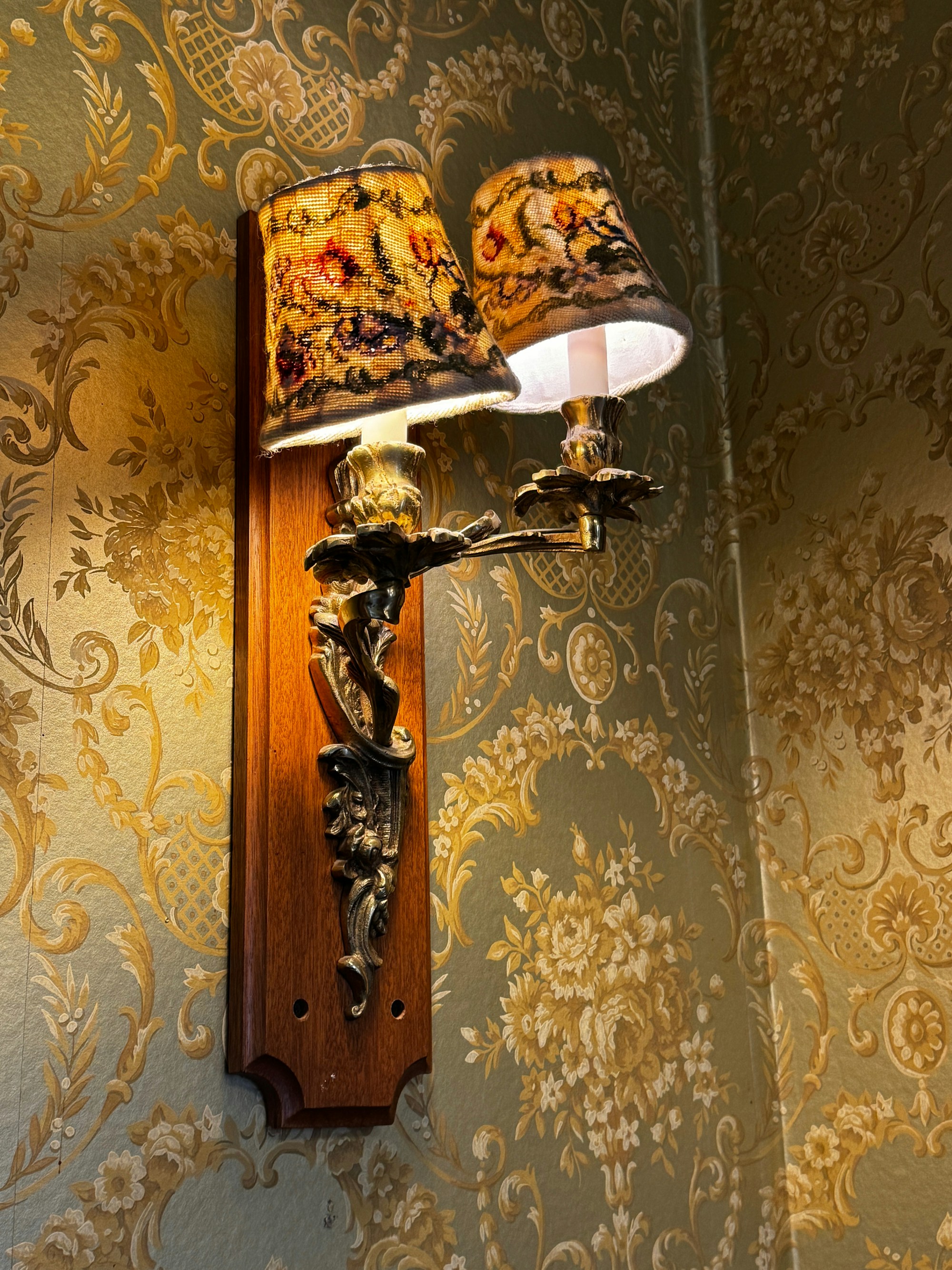 Decorative wall sconce mounted against textured wallpaper, casting a warm glow