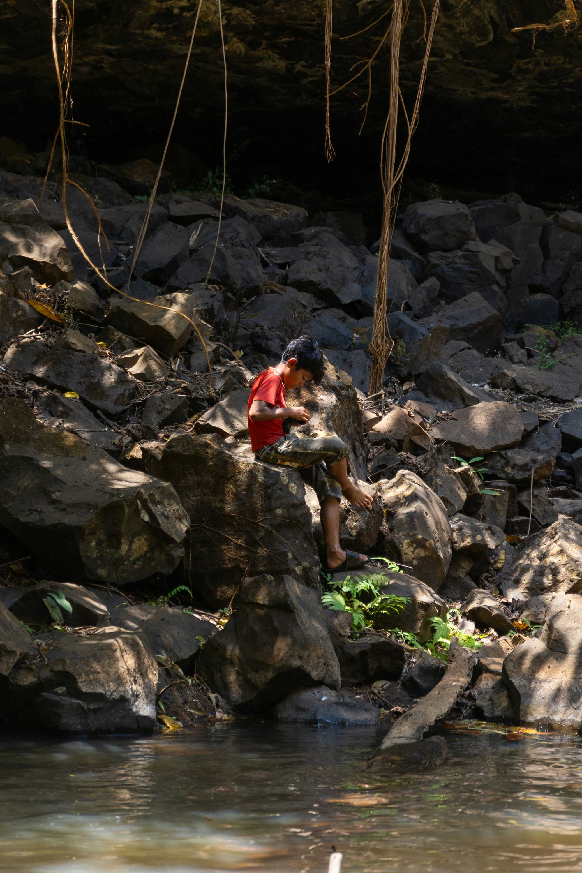 A child sits on rocks near the water.