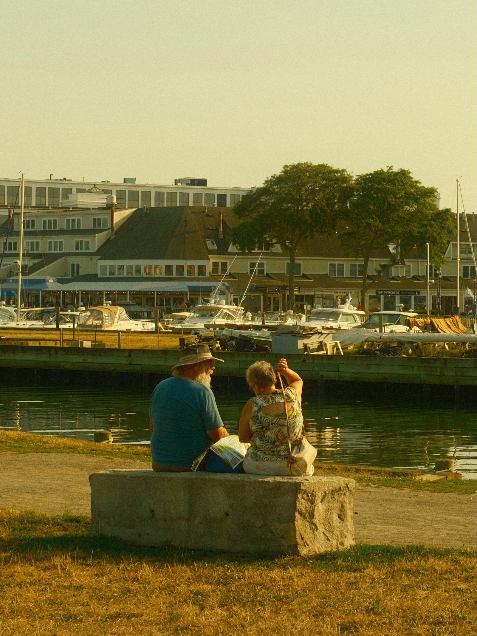 Two people sharing a bench beside Salem harbor in warm evening light