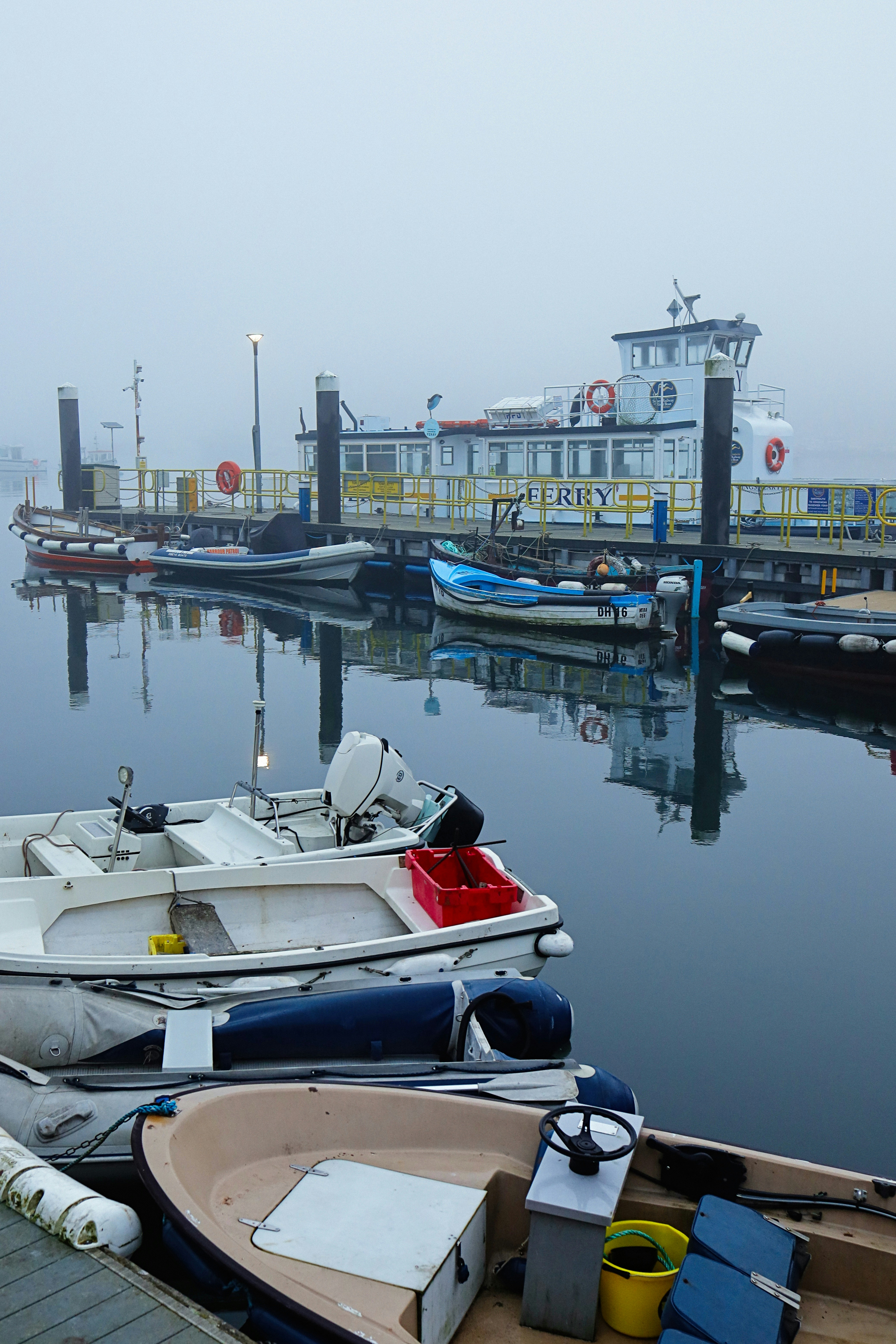 Boats are docked by a pier on a foggy morning.