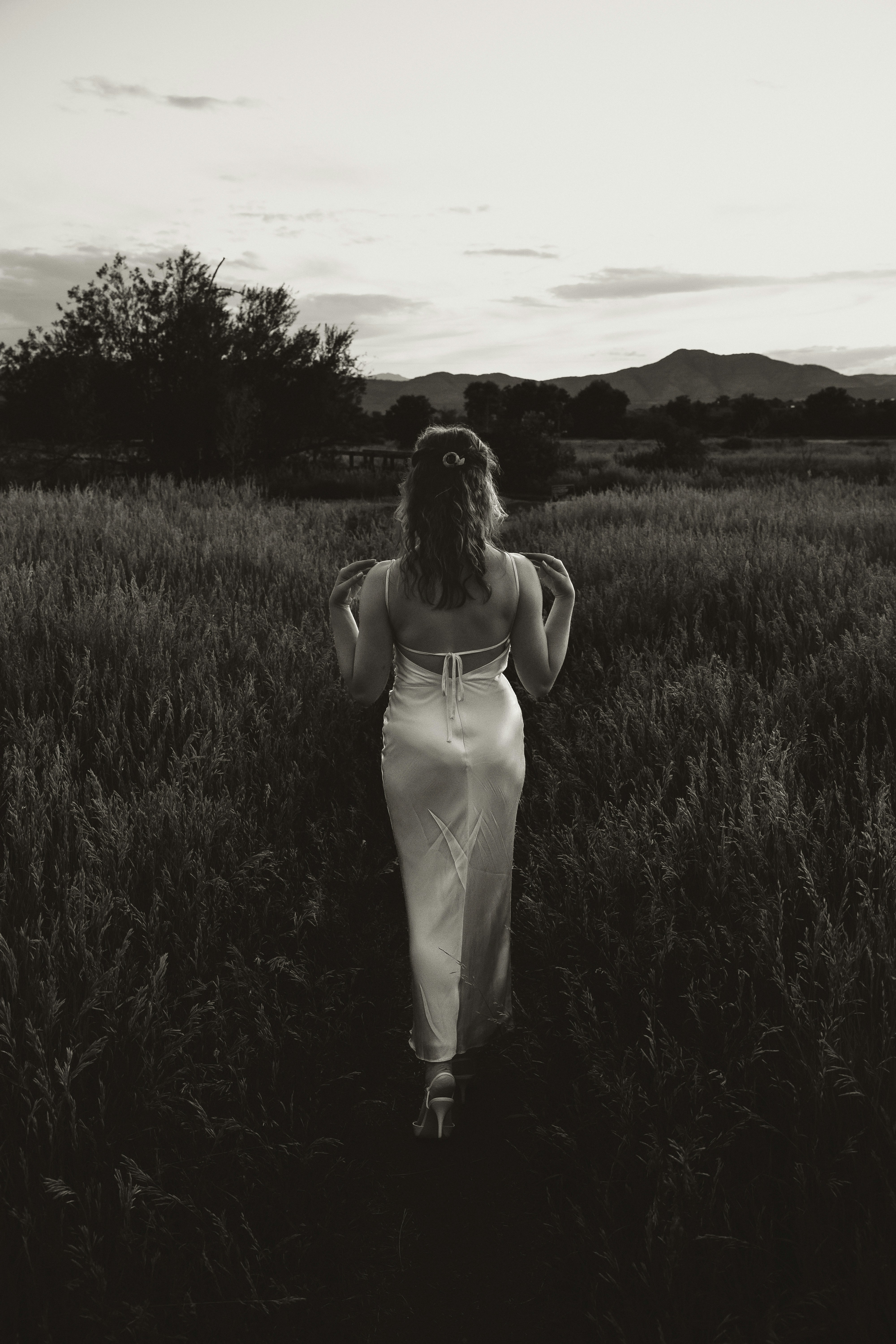 Woman walks away through tall grass, back to camera.
