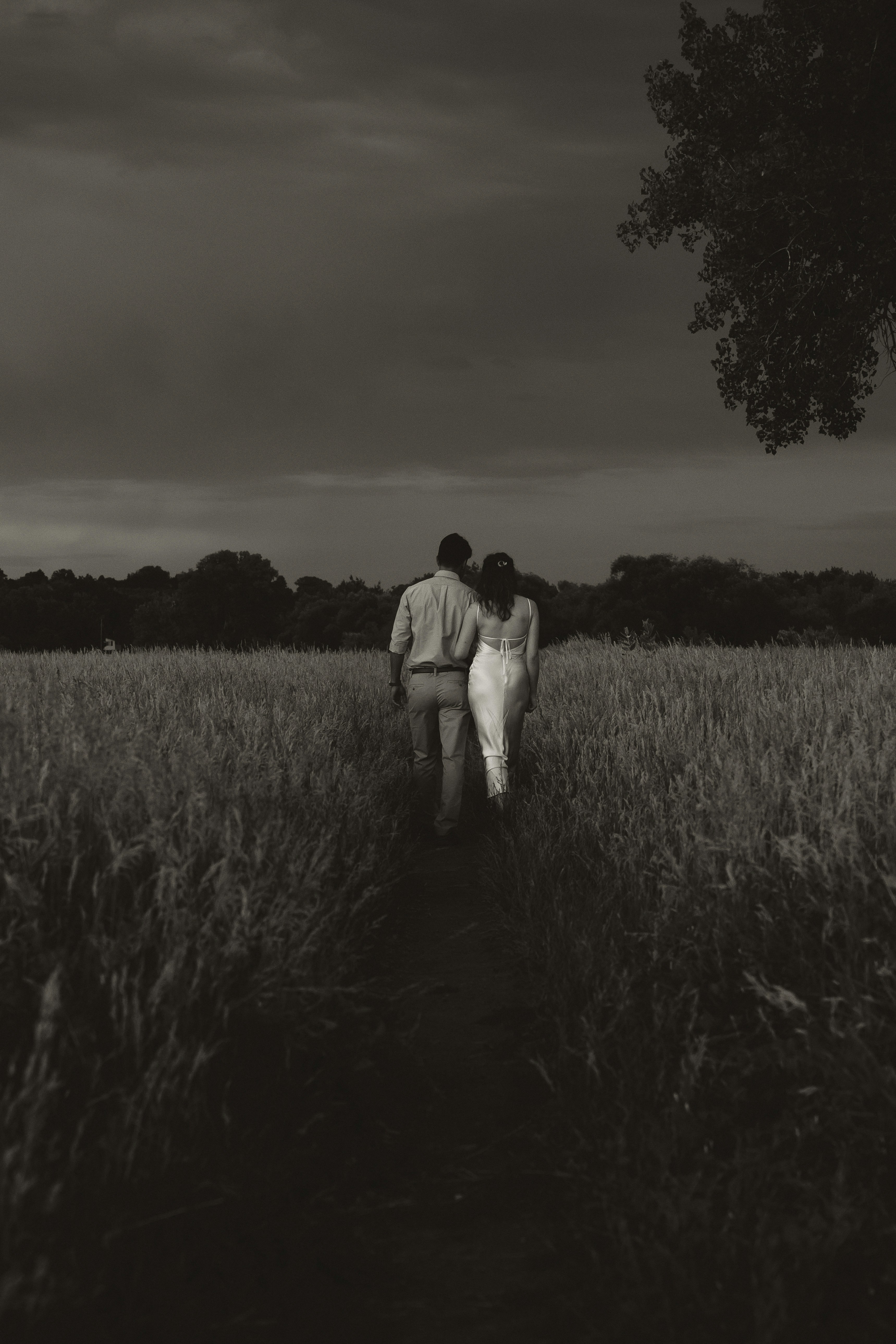 A couple walks through a field at dusk.