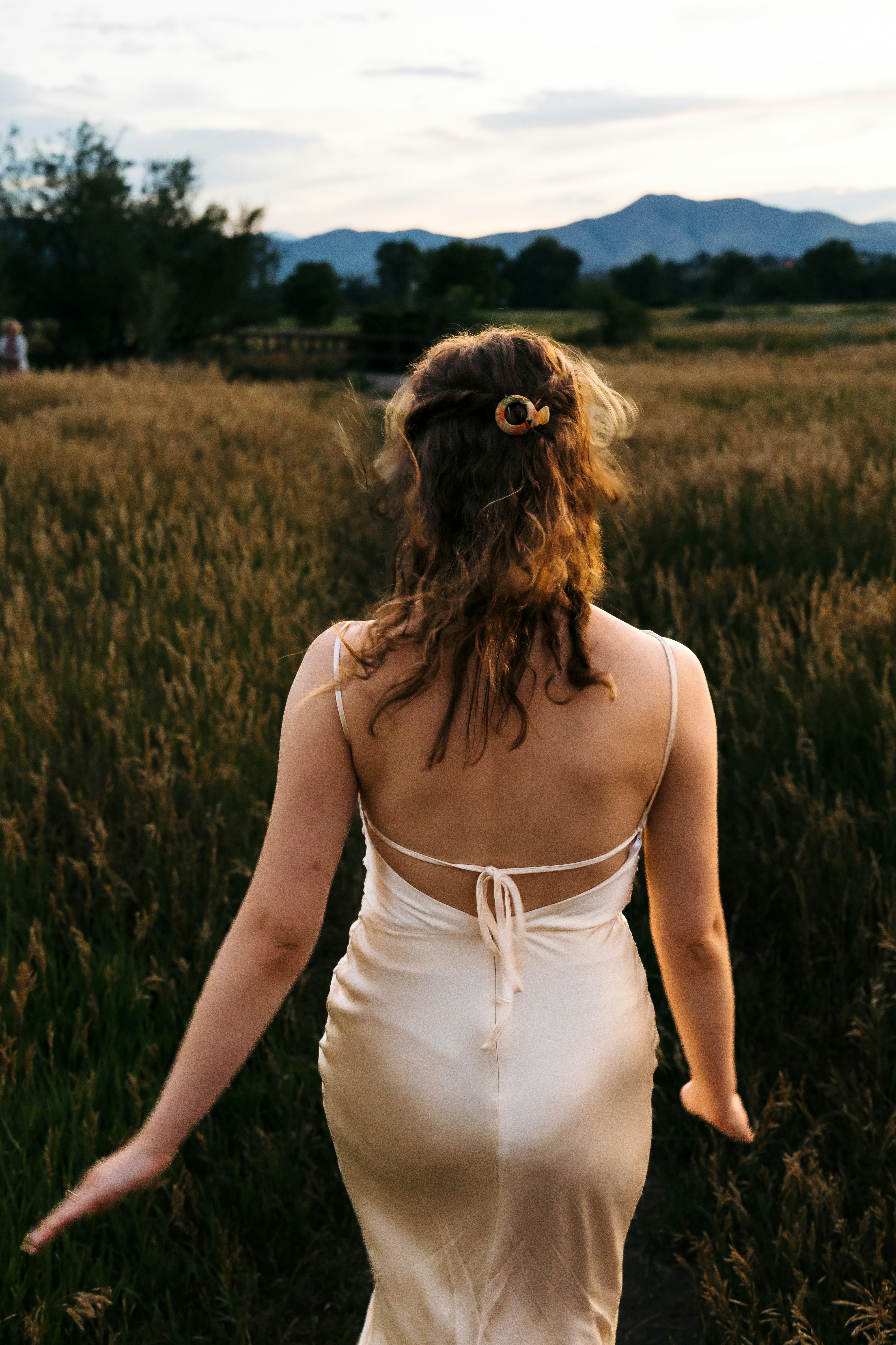 Woman walks through a field towards mountains.