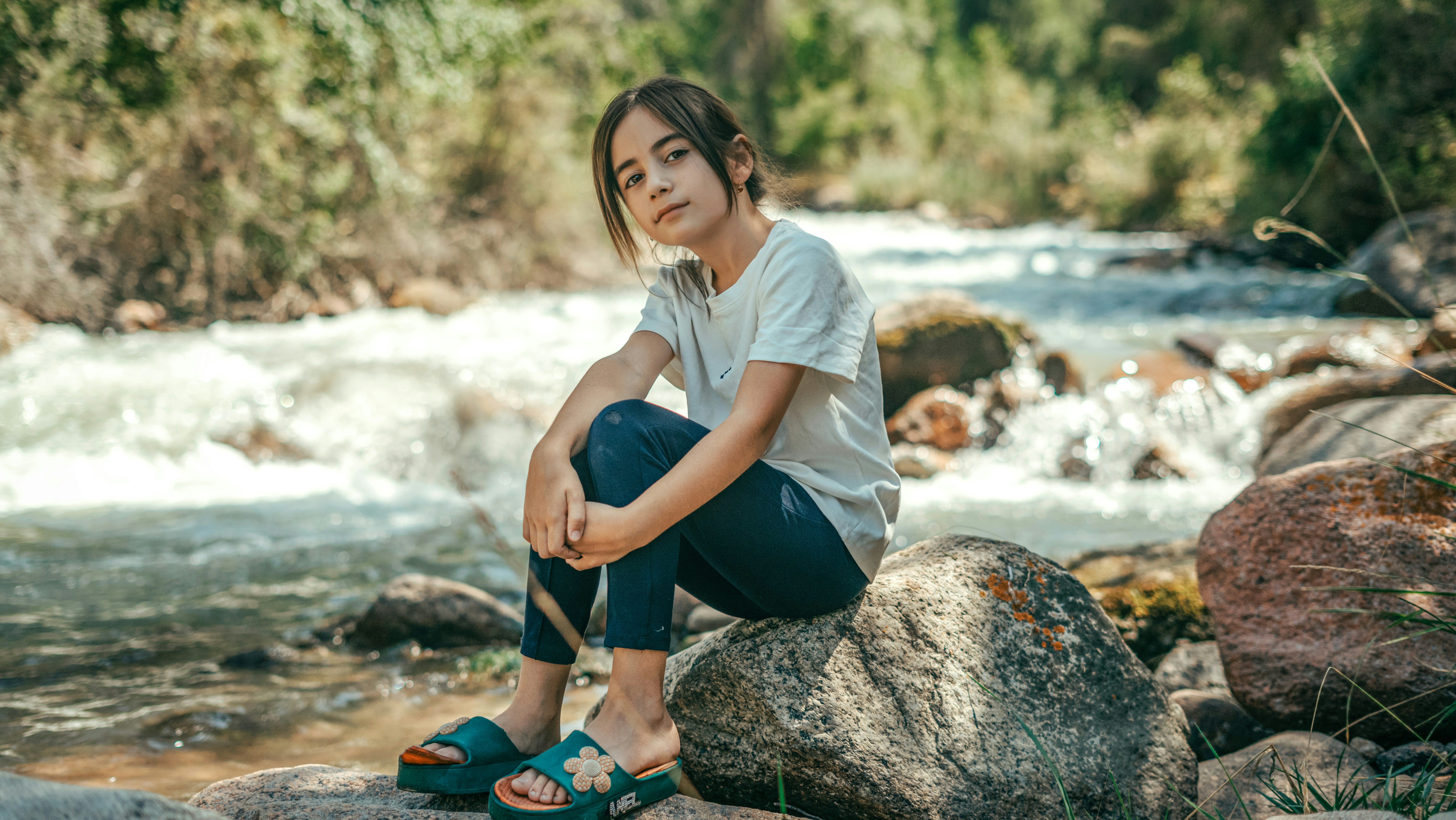 A girl sits on a rock near a rushing stream.