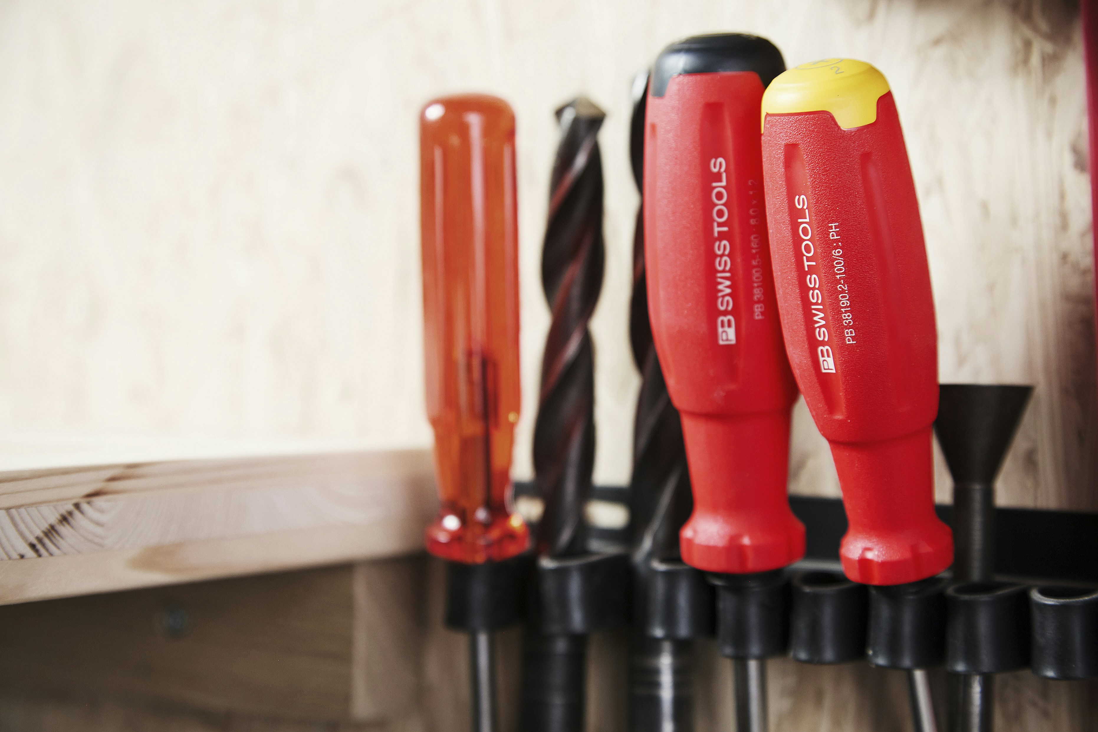 A variety of essential hand tools including a hammer, screwdriver, and tape measure arranged neatly on a wooden workbench in a bright home.
