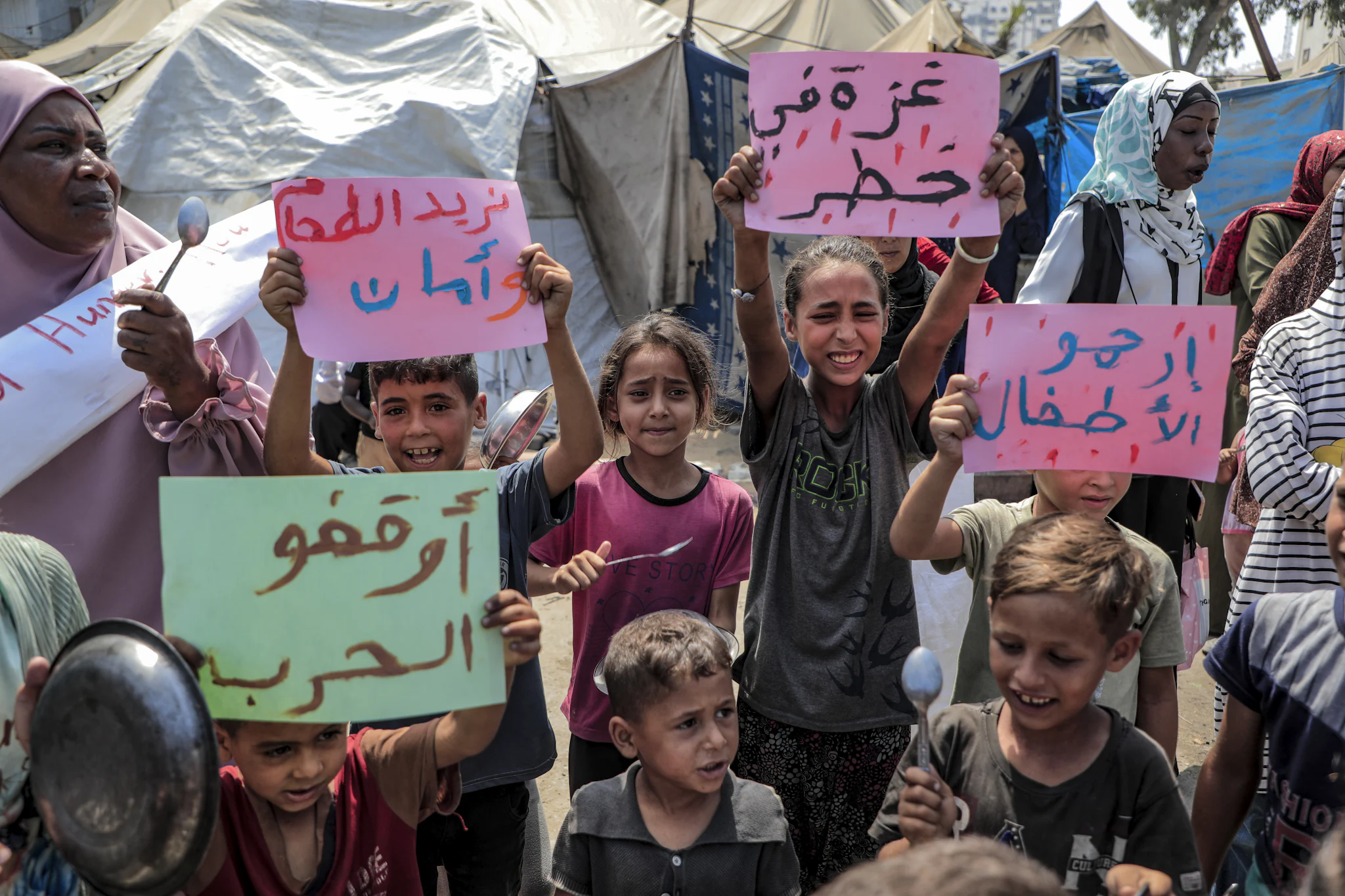 Children in Gaza bang empty pots as they walk through a sandy street, asking for food