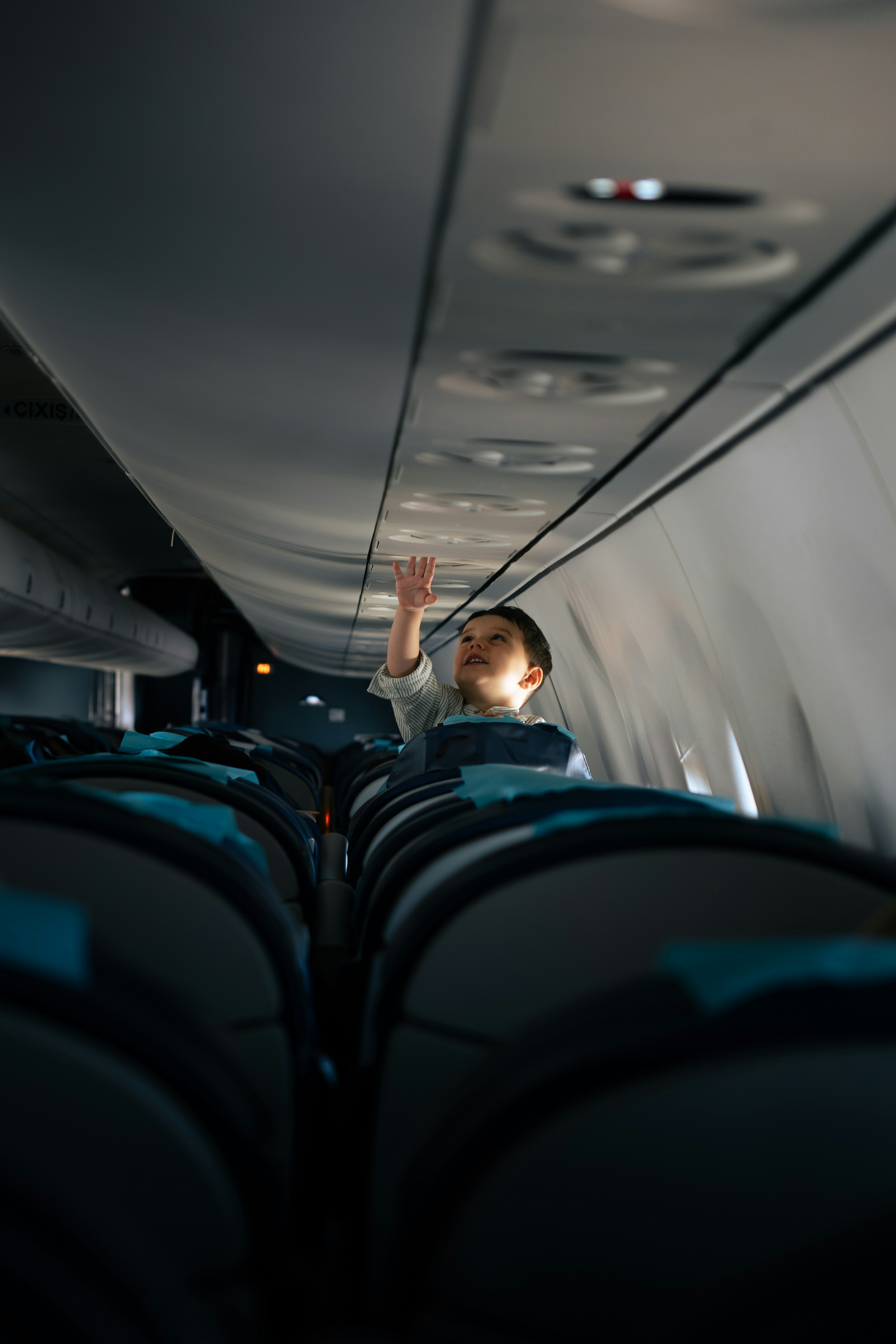 A child reaches for something on the airplane ceiling.