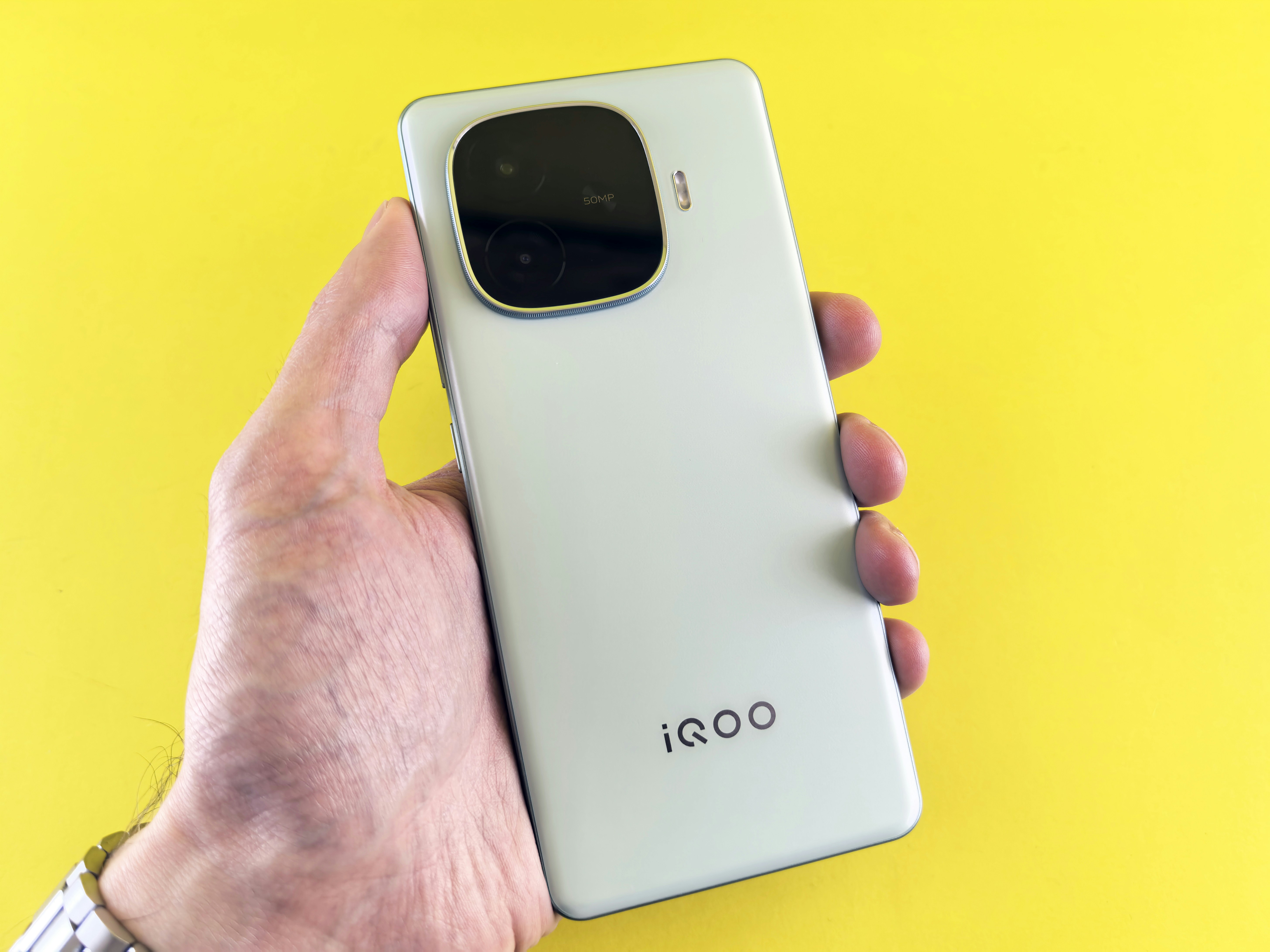 A hand holds an iqoo smartphone.