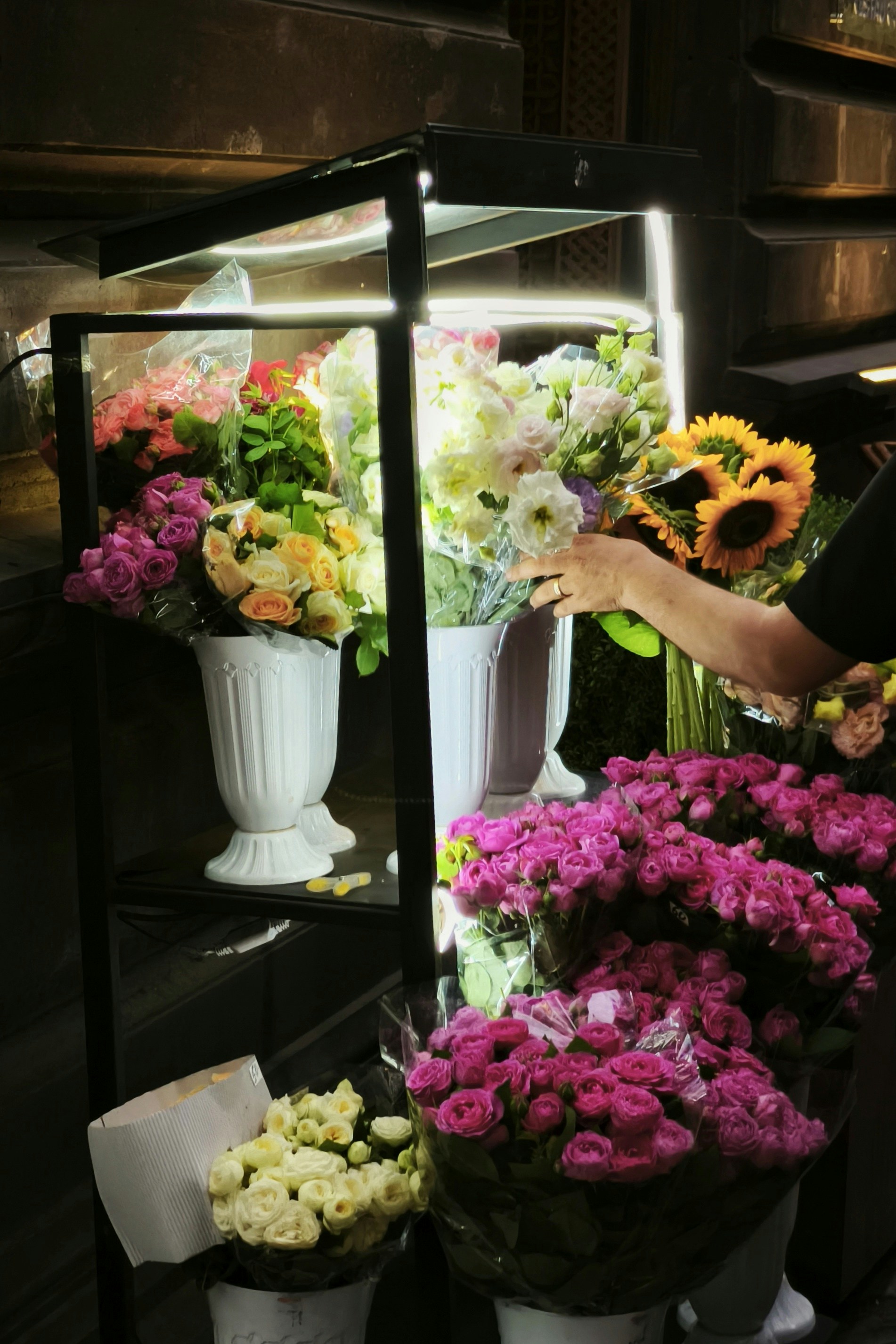 A person arranges flowers in a brightly lit display.