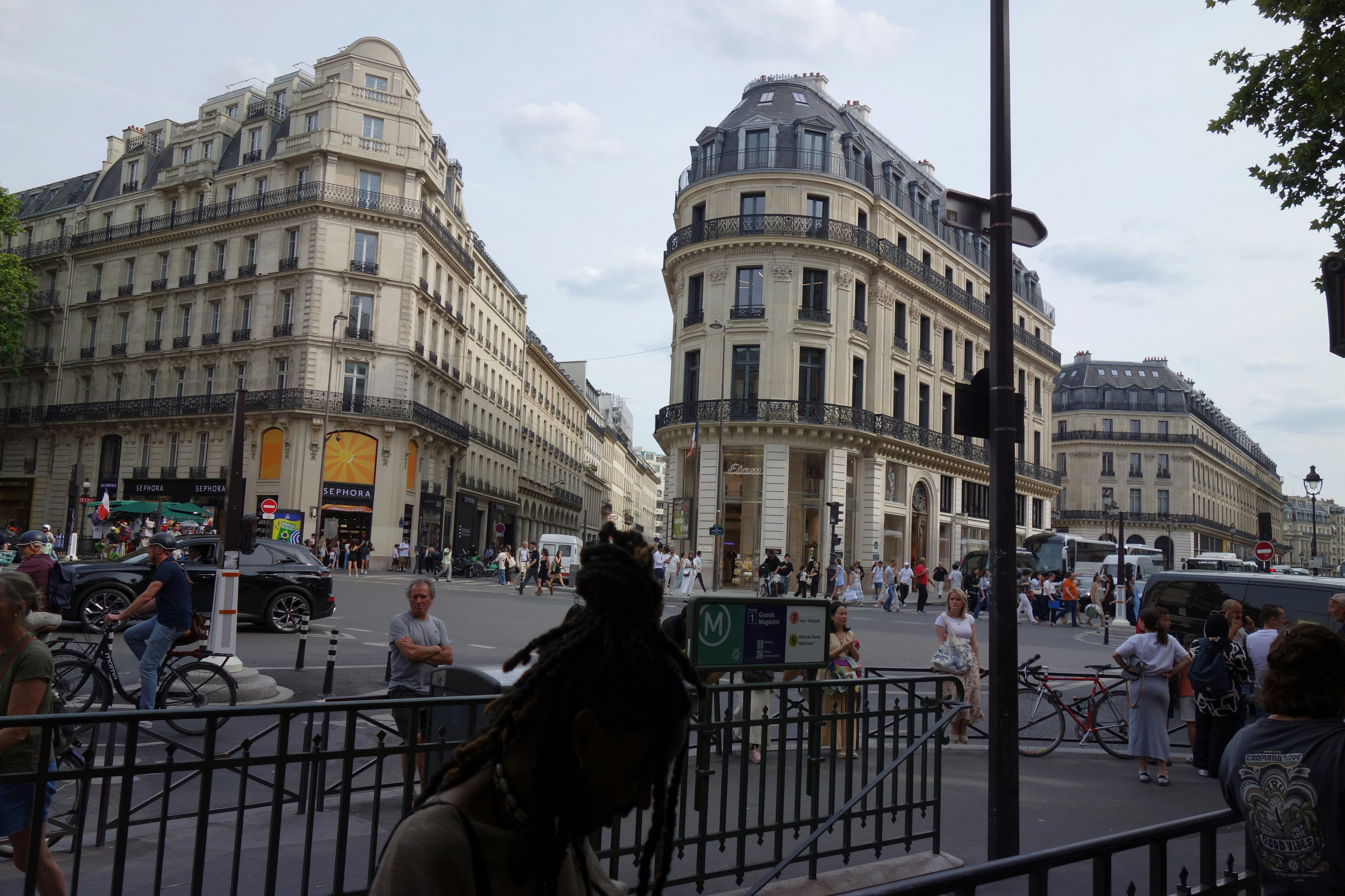 Parisian buildings and people fill a city street.