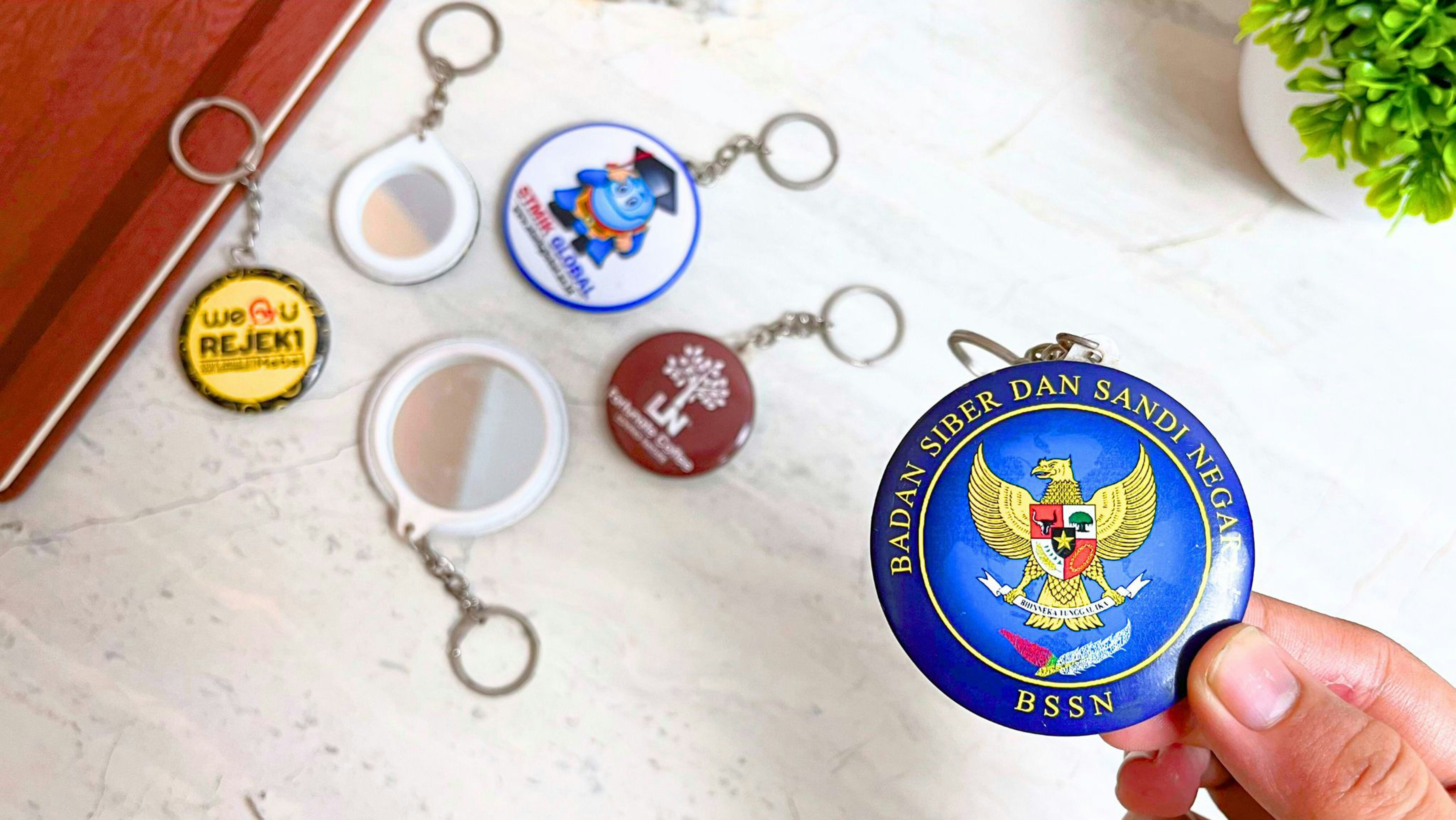 A hand holds a blue keychain over a marble desk.