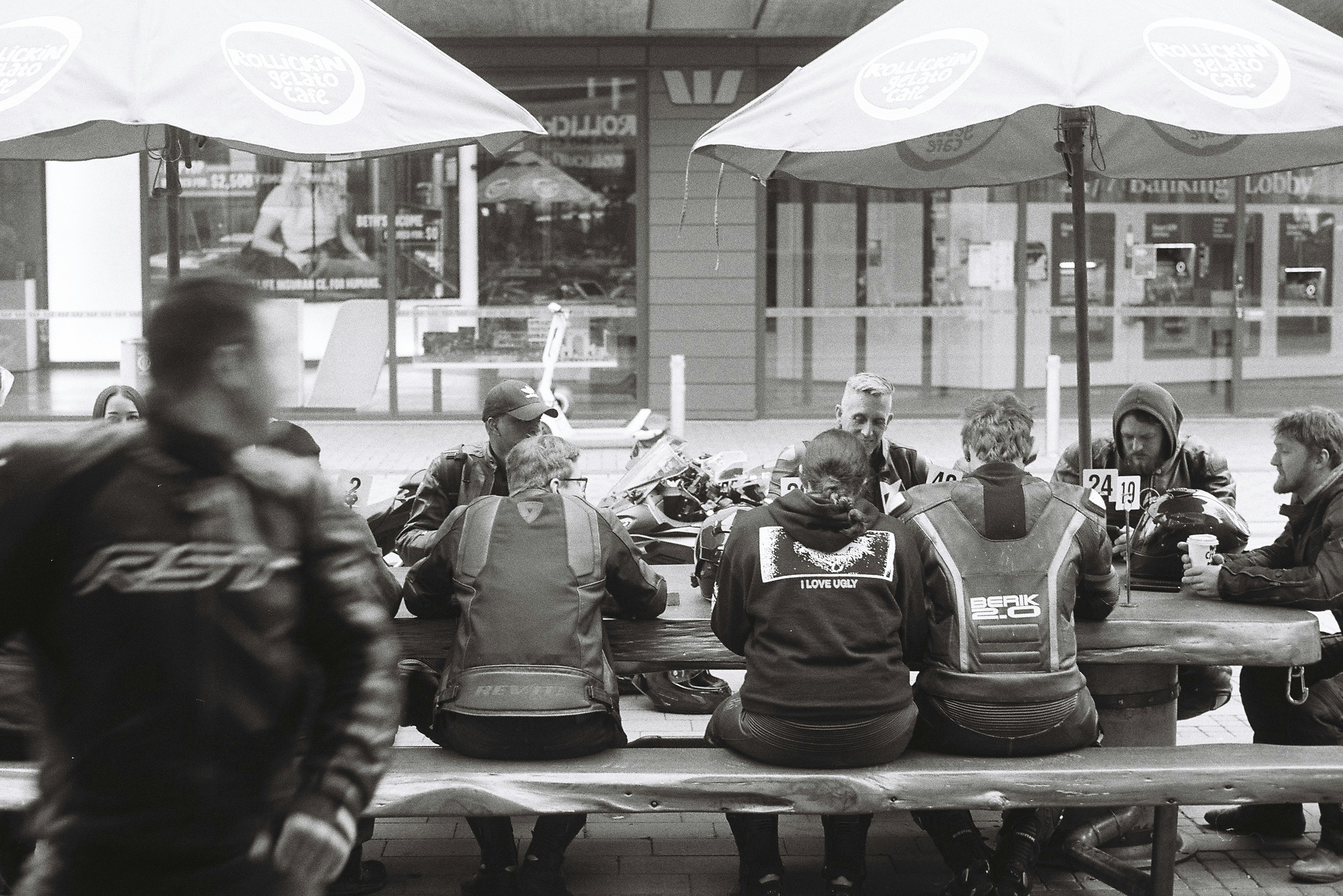 Motorcyclists sit at an outdoor table in a café.