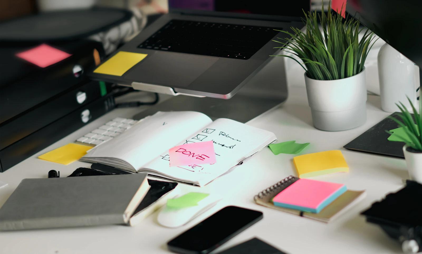 A desk with a planner, sticky notes and a laptop
