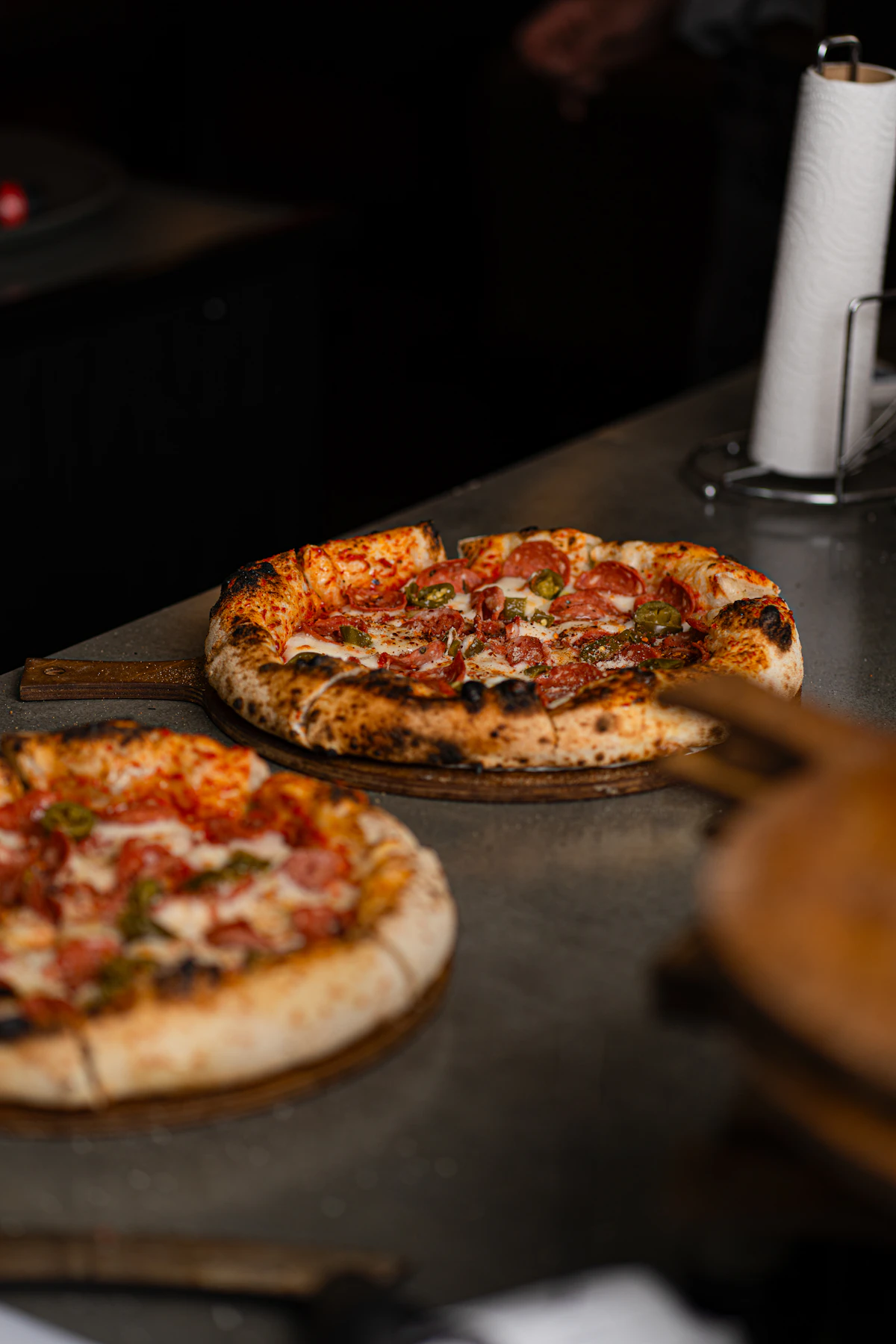 Two finished pizzas resting on a steel counter, ready to be cut