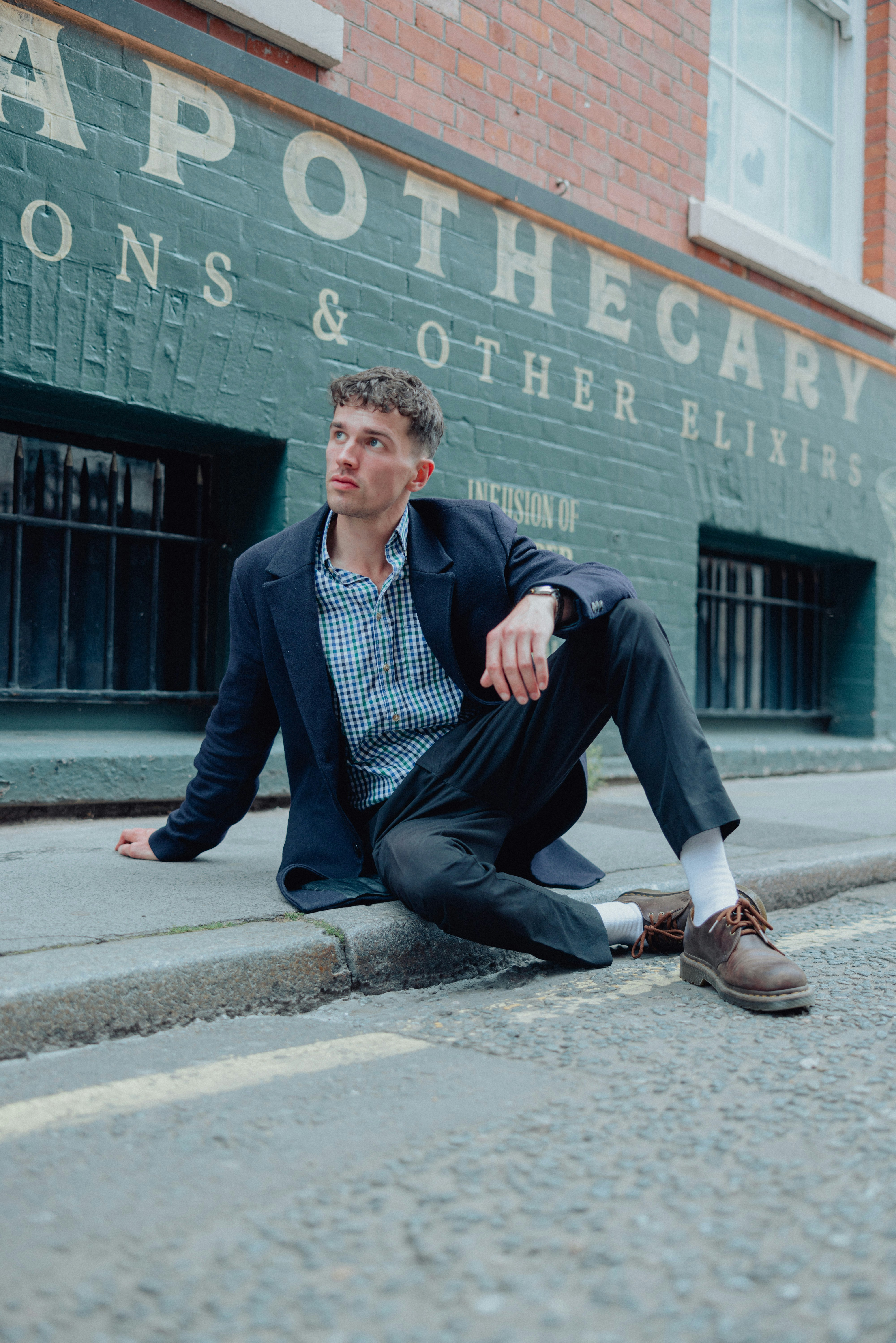 Man poses on the curb in front of apothecary.