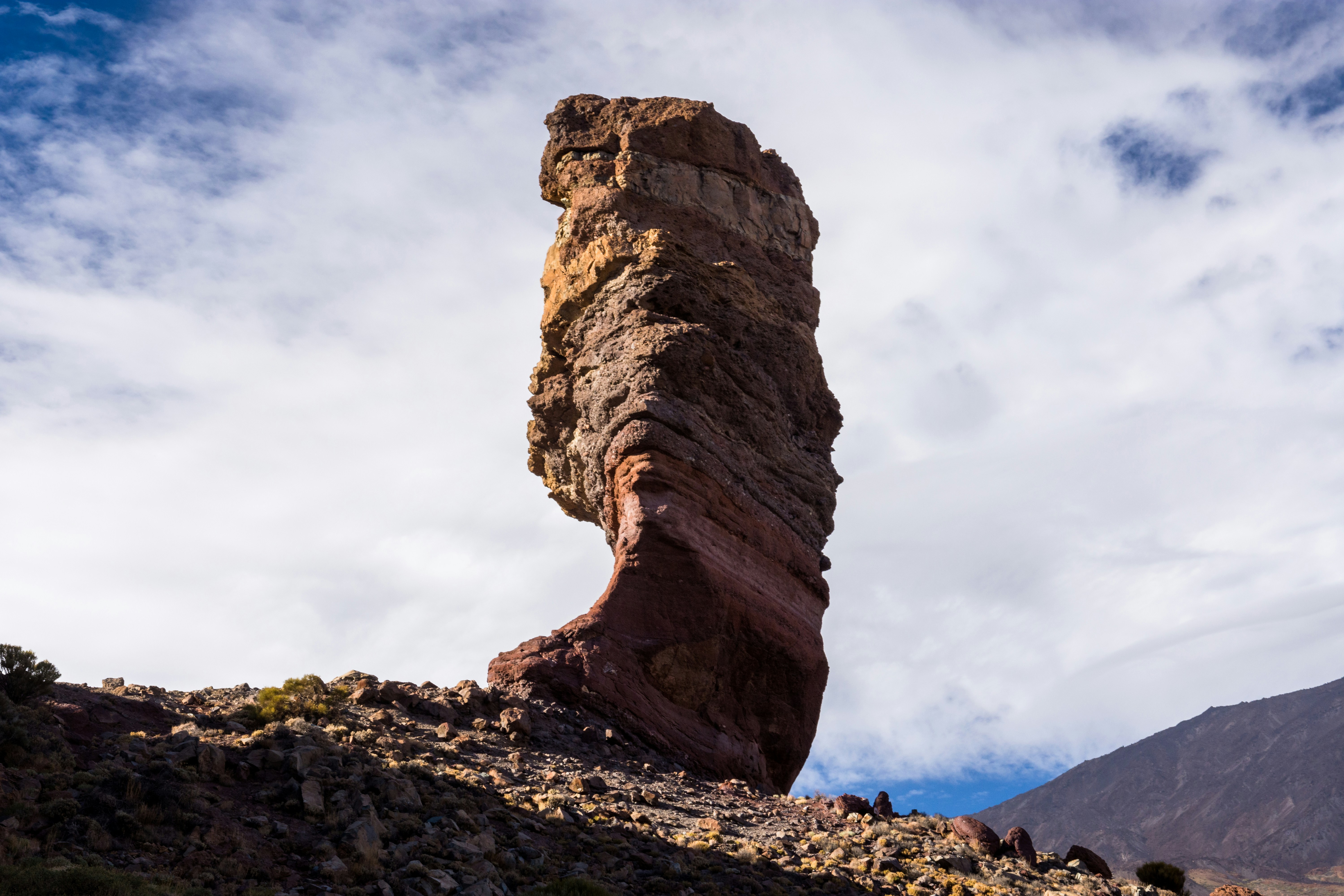 A tall, layered rock formation against clouds.
