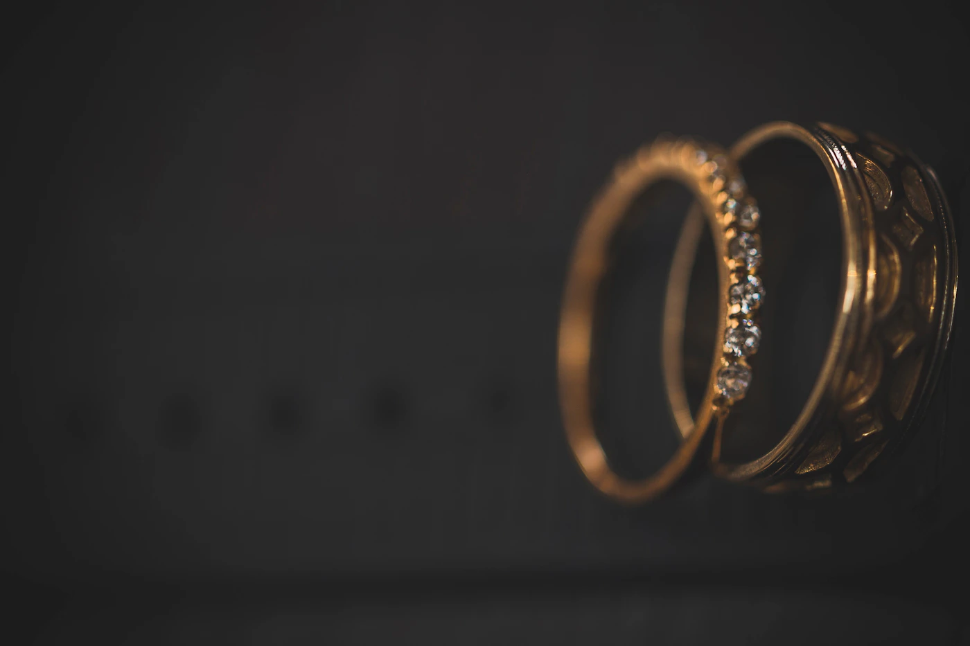 Golden wedding rings gleaming against a dark background showing the ring detail photography that captures these objects at their most isolated and specific before they are worn