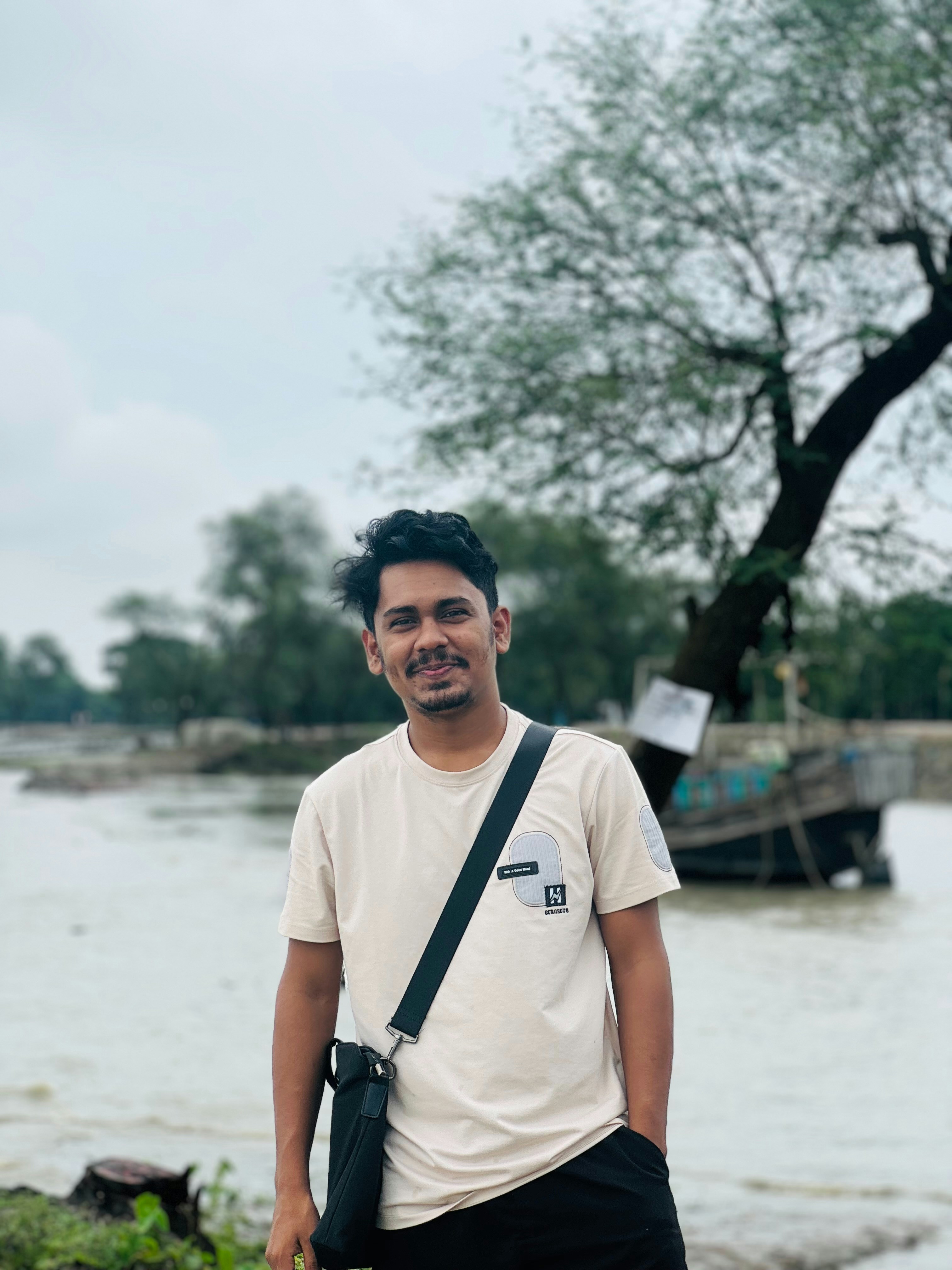 Seorang pria berdiri di tepi sungai yang terendam banjir dengan pohon.