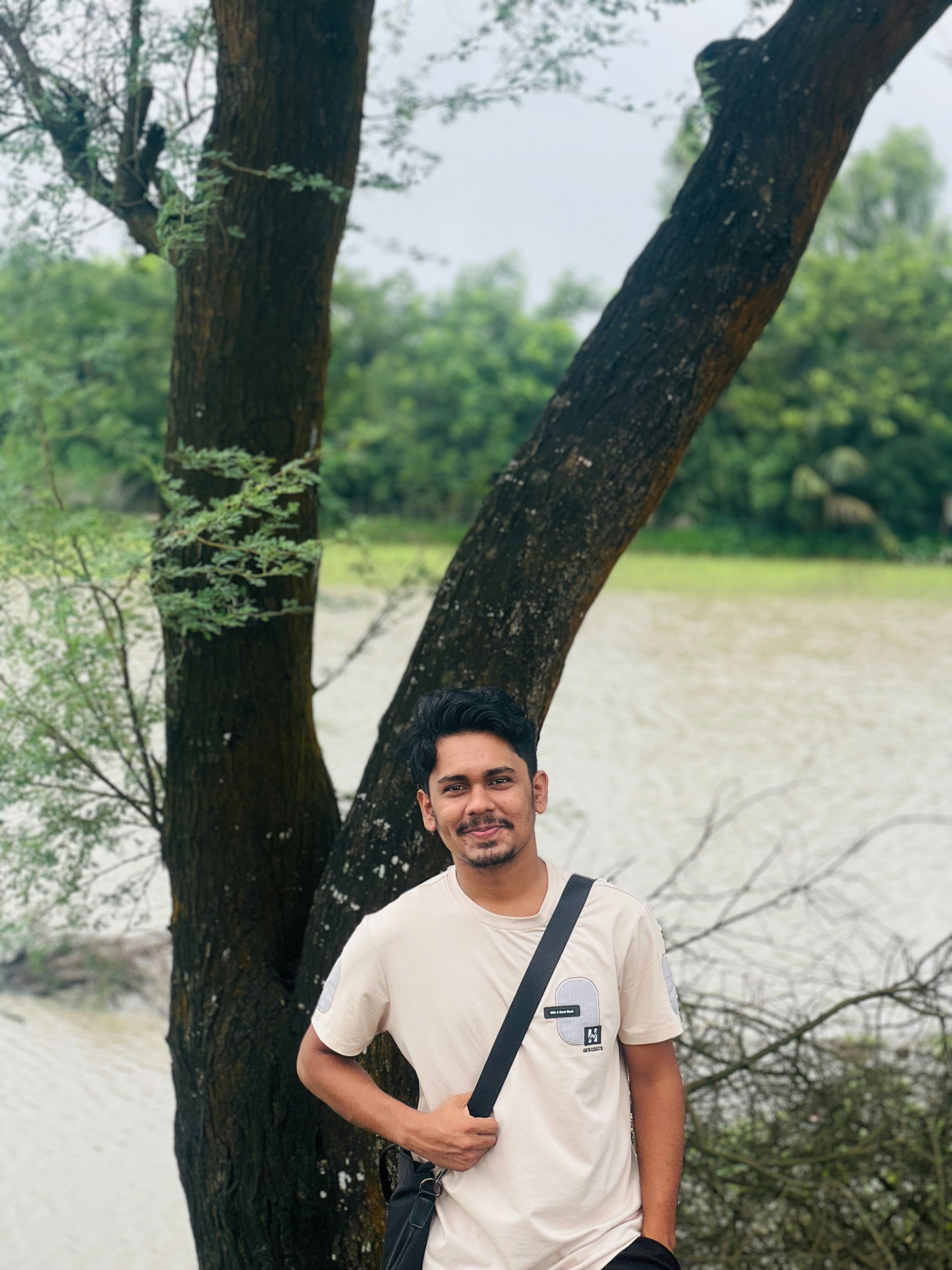 水辺の木のそばで微笑む青年。