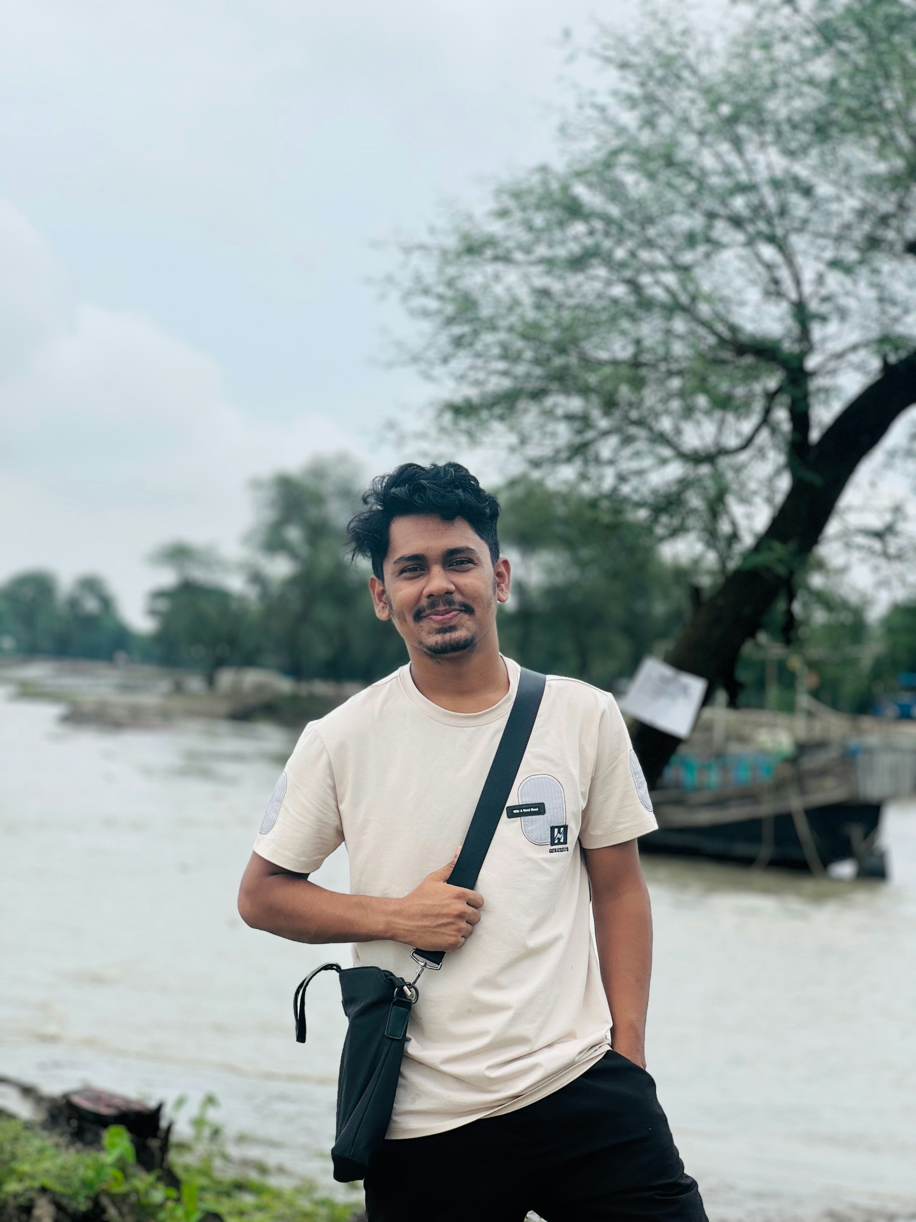 Pemuda dengan tas selempang di tepi sungai.