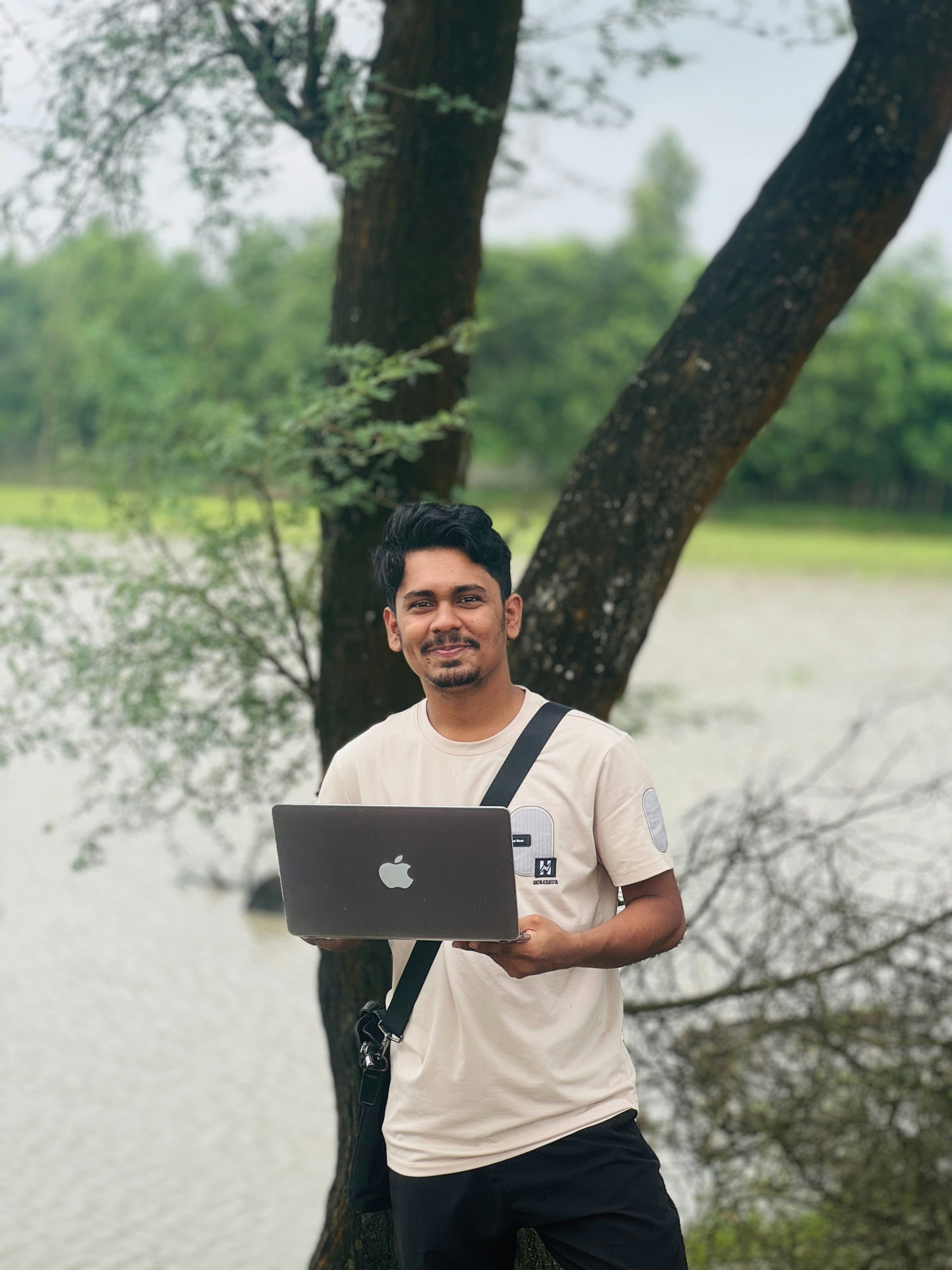 Hombre sosteniendo una computadora portátil al aire libre cerca de un árbol