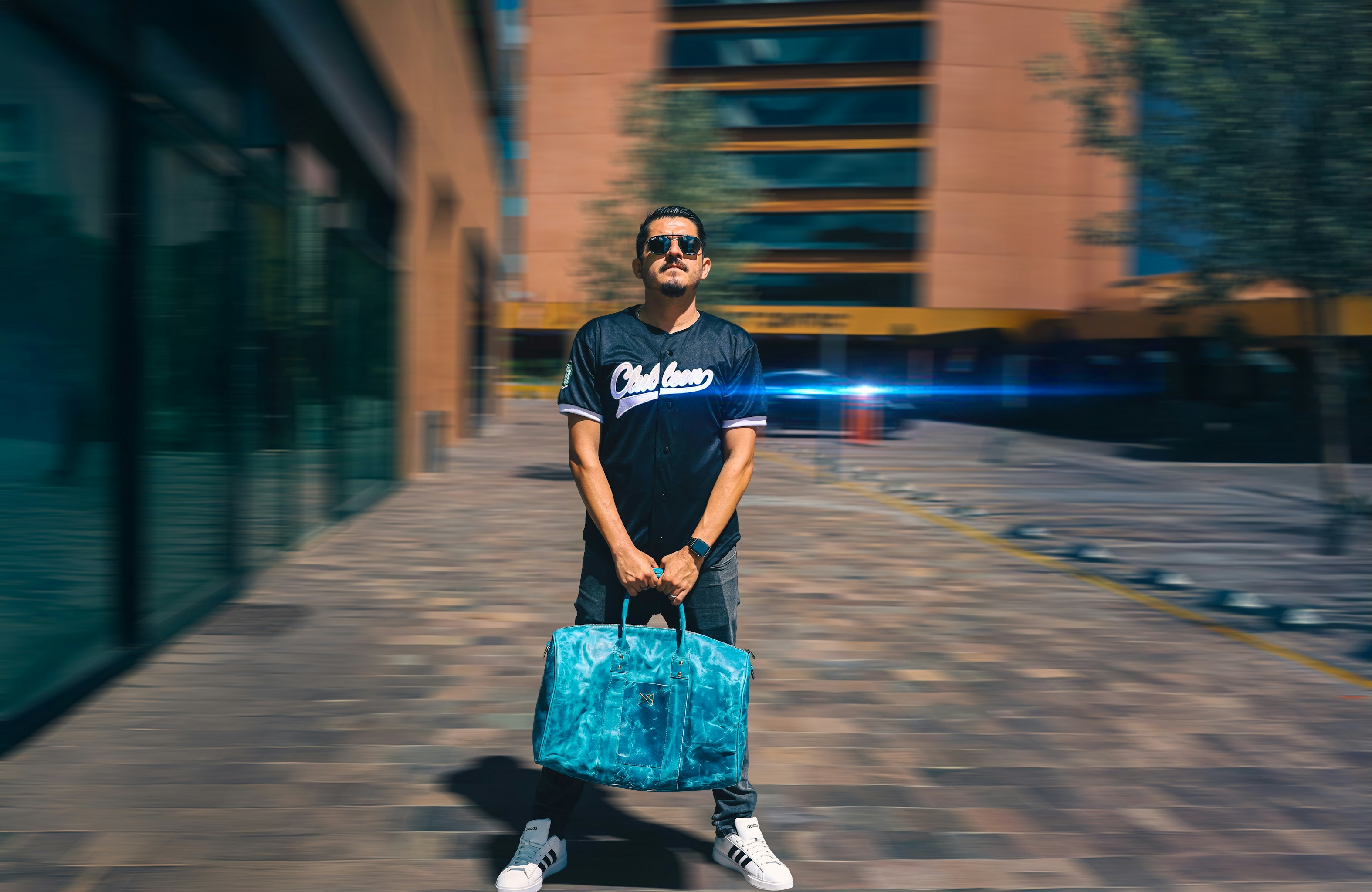 A man poses with a bag in front of buildings.