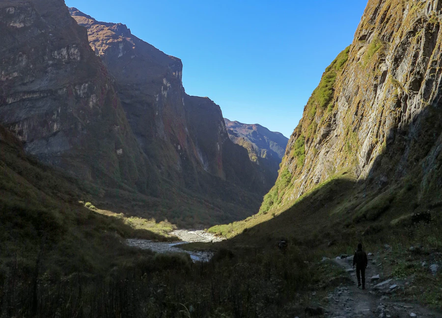 A person walking alone through a mountain valley beneath dramatic light