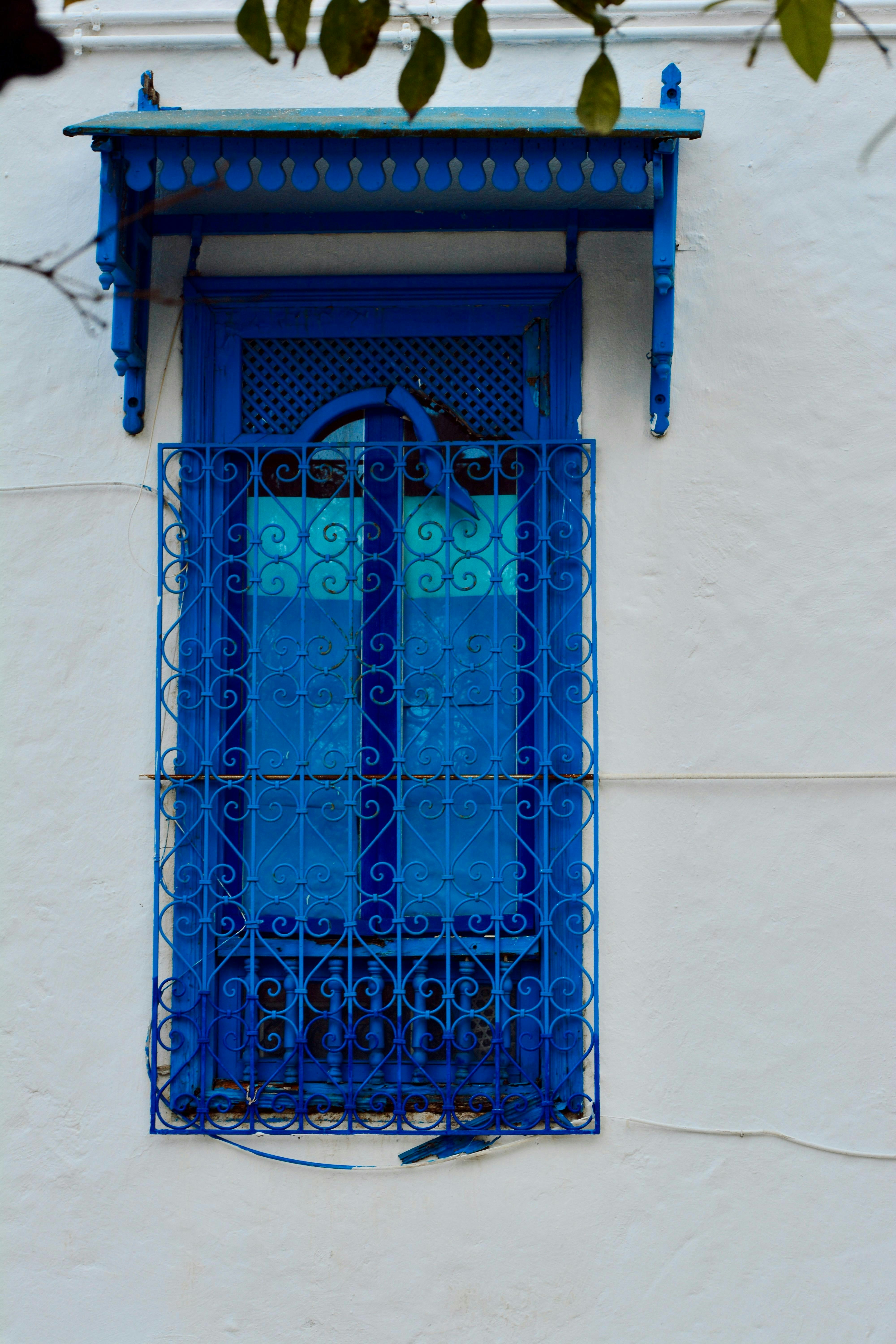 Blue window with elaborate detailing on a white wall.