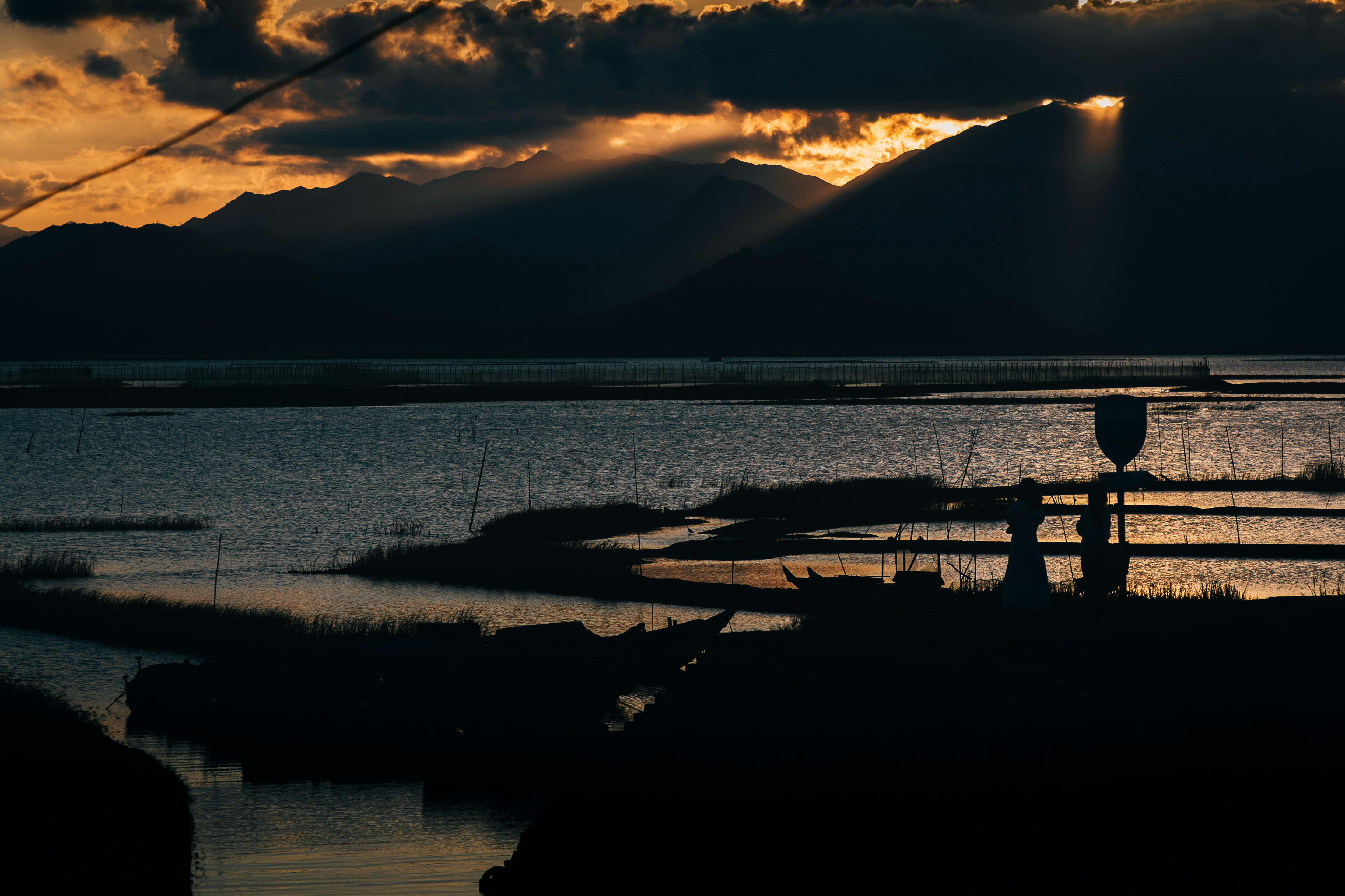 Os raios de sol iluminam um lago escuro e montanhas.